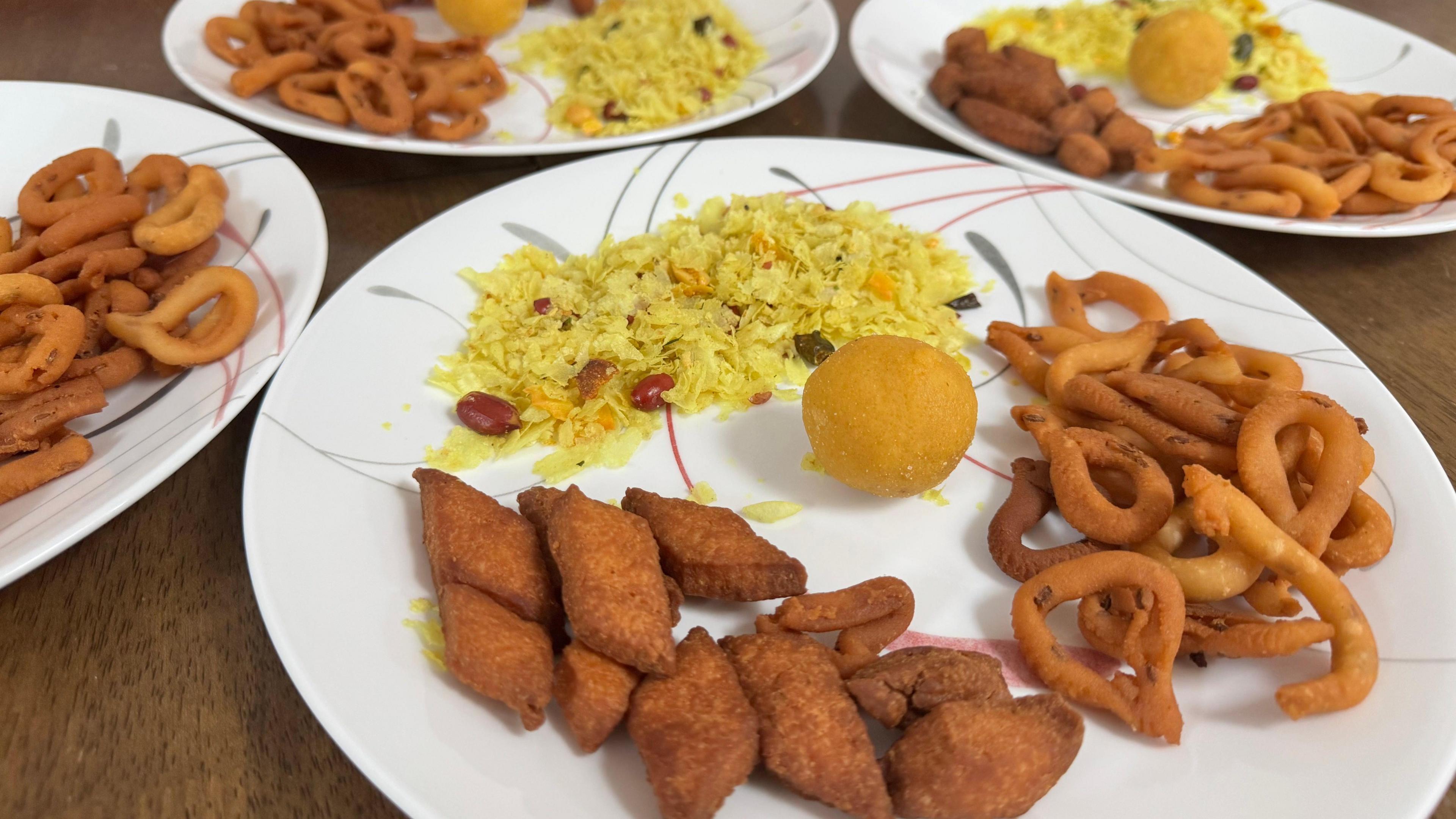 Four plates with a laddoo or Indian sweet and three other savoury snacks. 