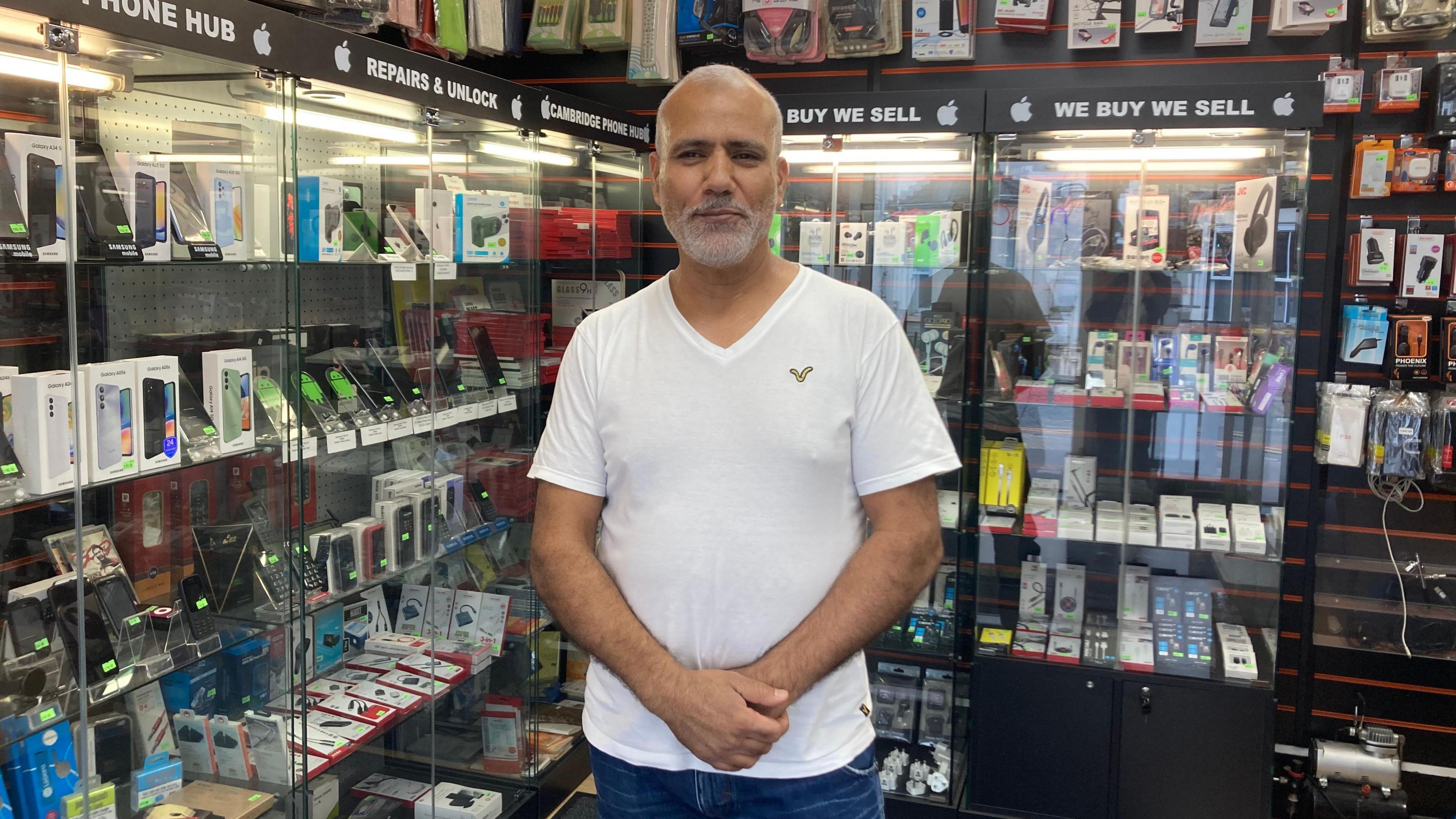 Ezedeen standing by a cabinet of phone cases in his shop