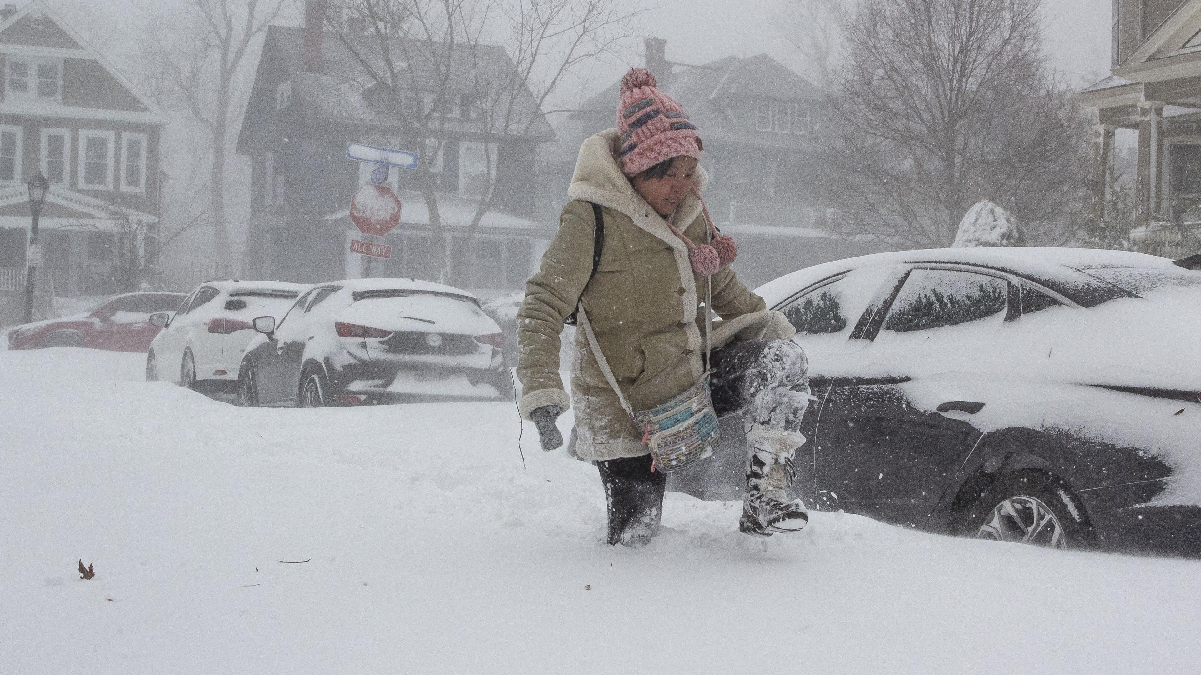 A woman walks through knee-deep snow on an urban street