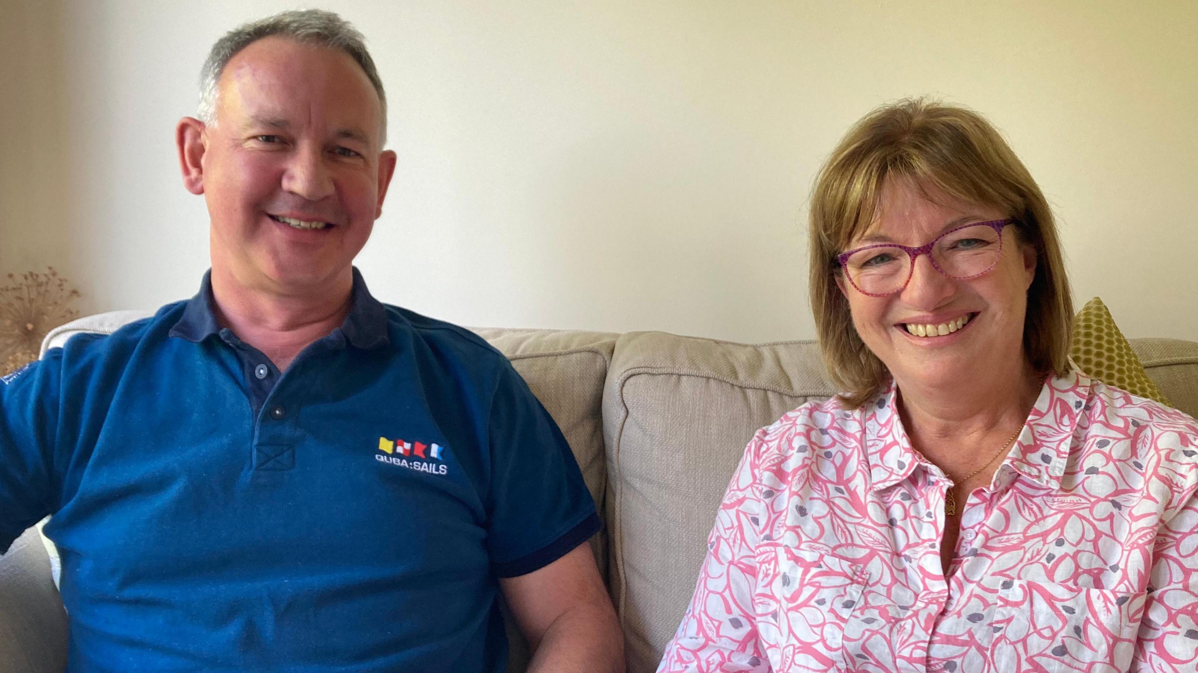 Ed Lowe's parents David, sat on the left of a settee with a blue T-shirt on smiling next to wife Hilary, who is wearing a pink floral shirt and also wearing pink glasses