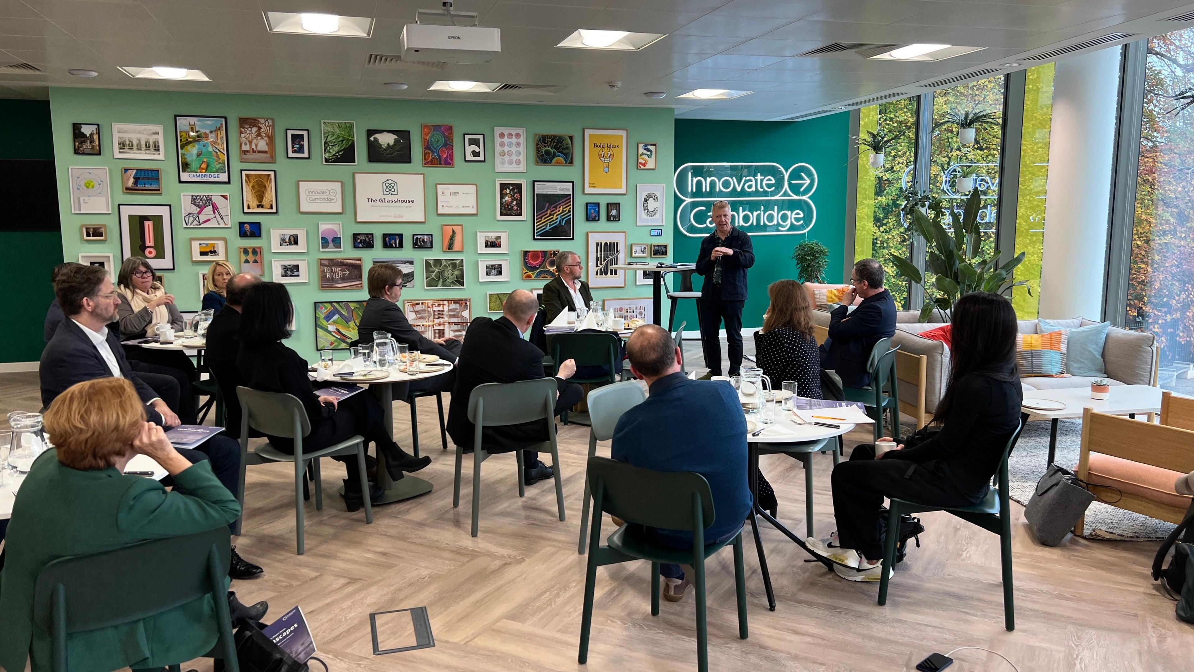 People gathered at tables in a meeting room with large windows and lots of pictures on green-painted walls