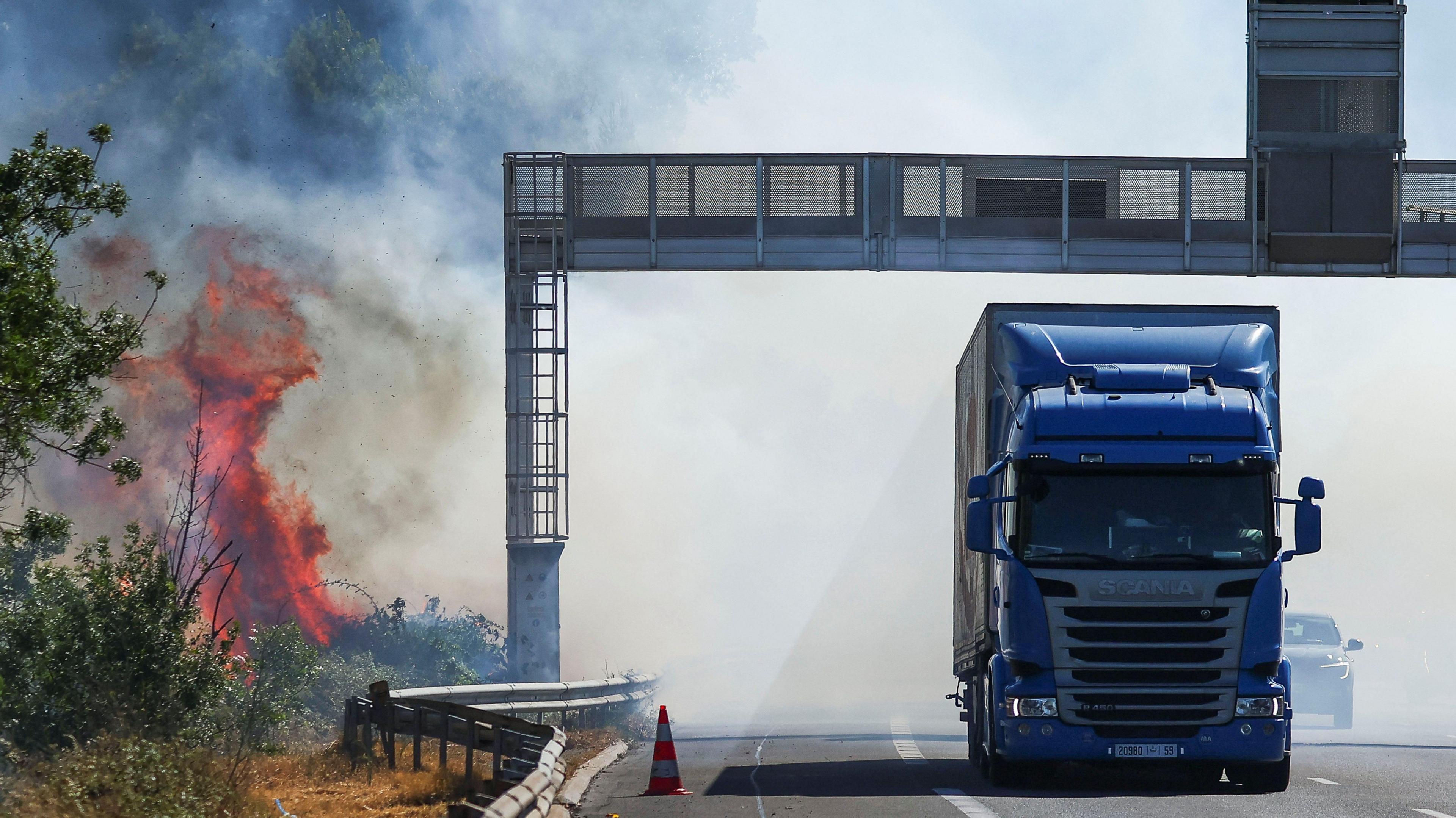 A truck drives next to a fire as a firefighting plane (not pictured) flies to battle wildfire near the A9 motorway near Beziers, France, July 3, 2026. 
