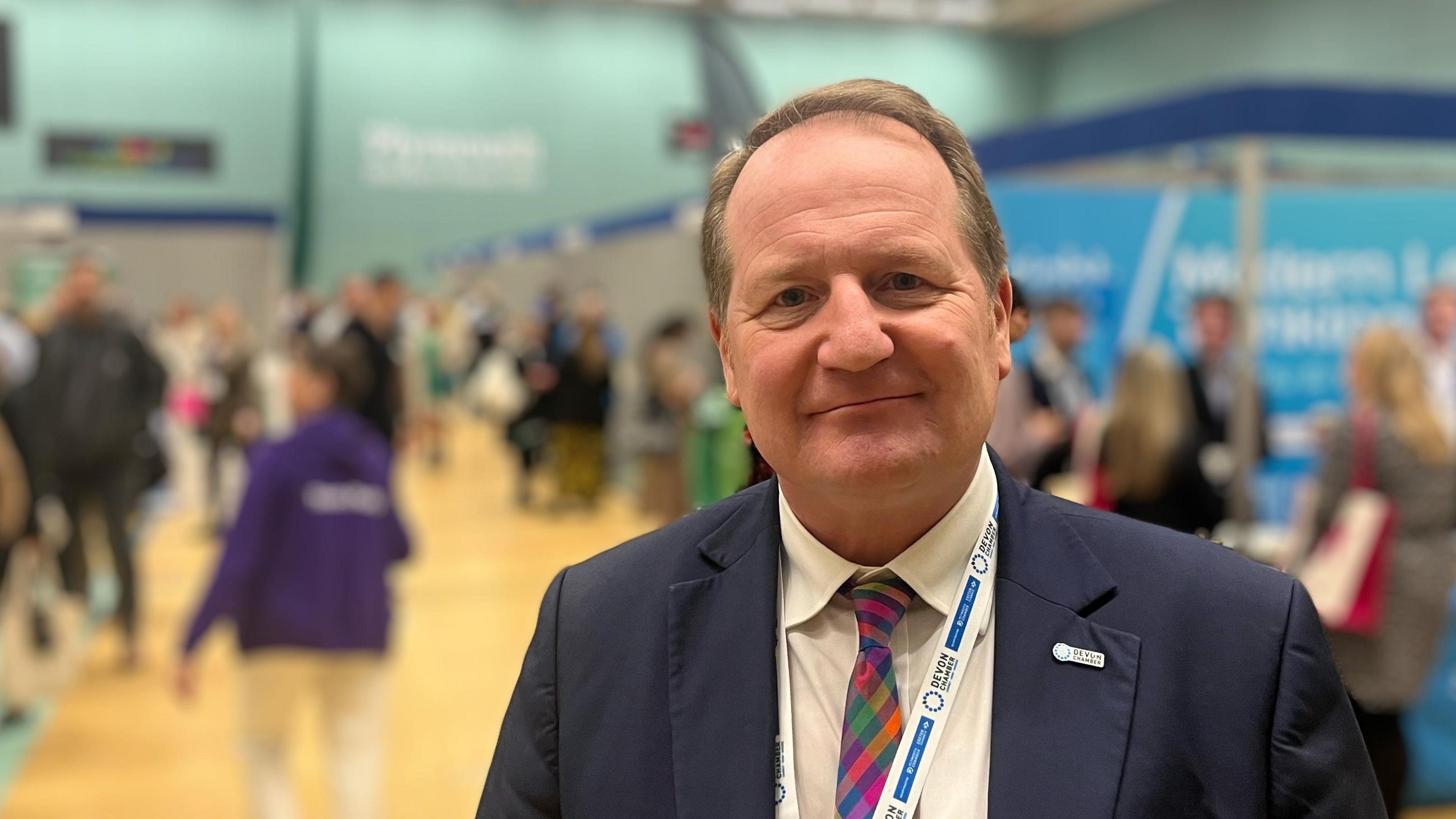 Stuart Elford wearing a blue jacket and multi-coloured tie with a blurred background at the Devon Business Show