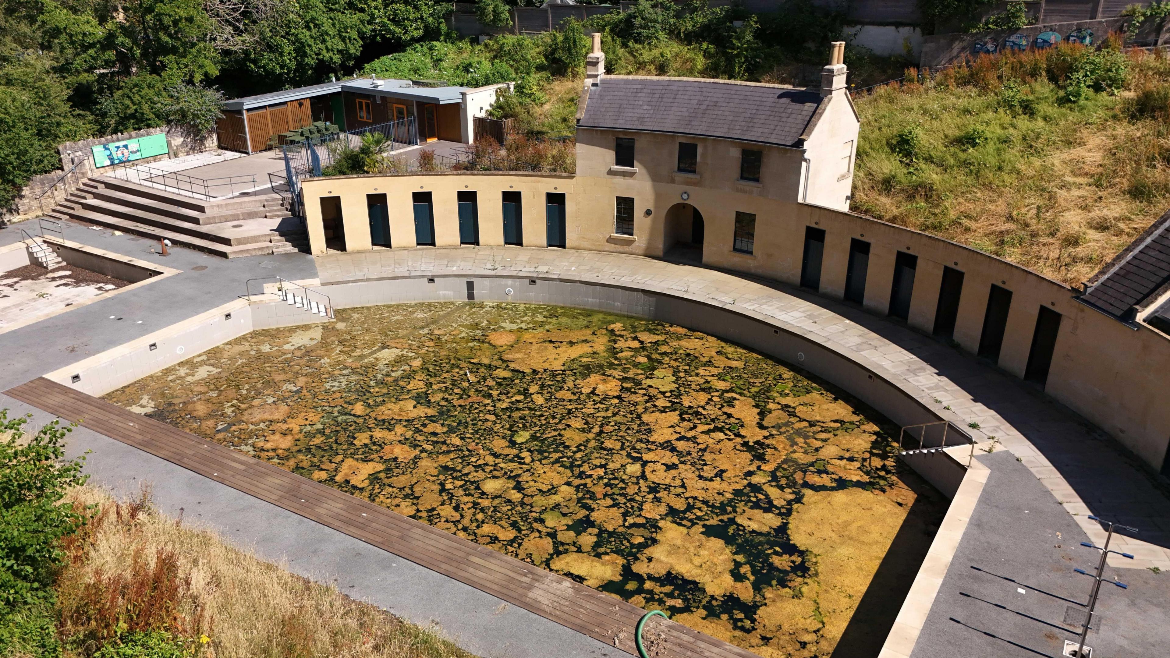 Drone footage of an old lido. It looks renovated but is full of algae in the pool.