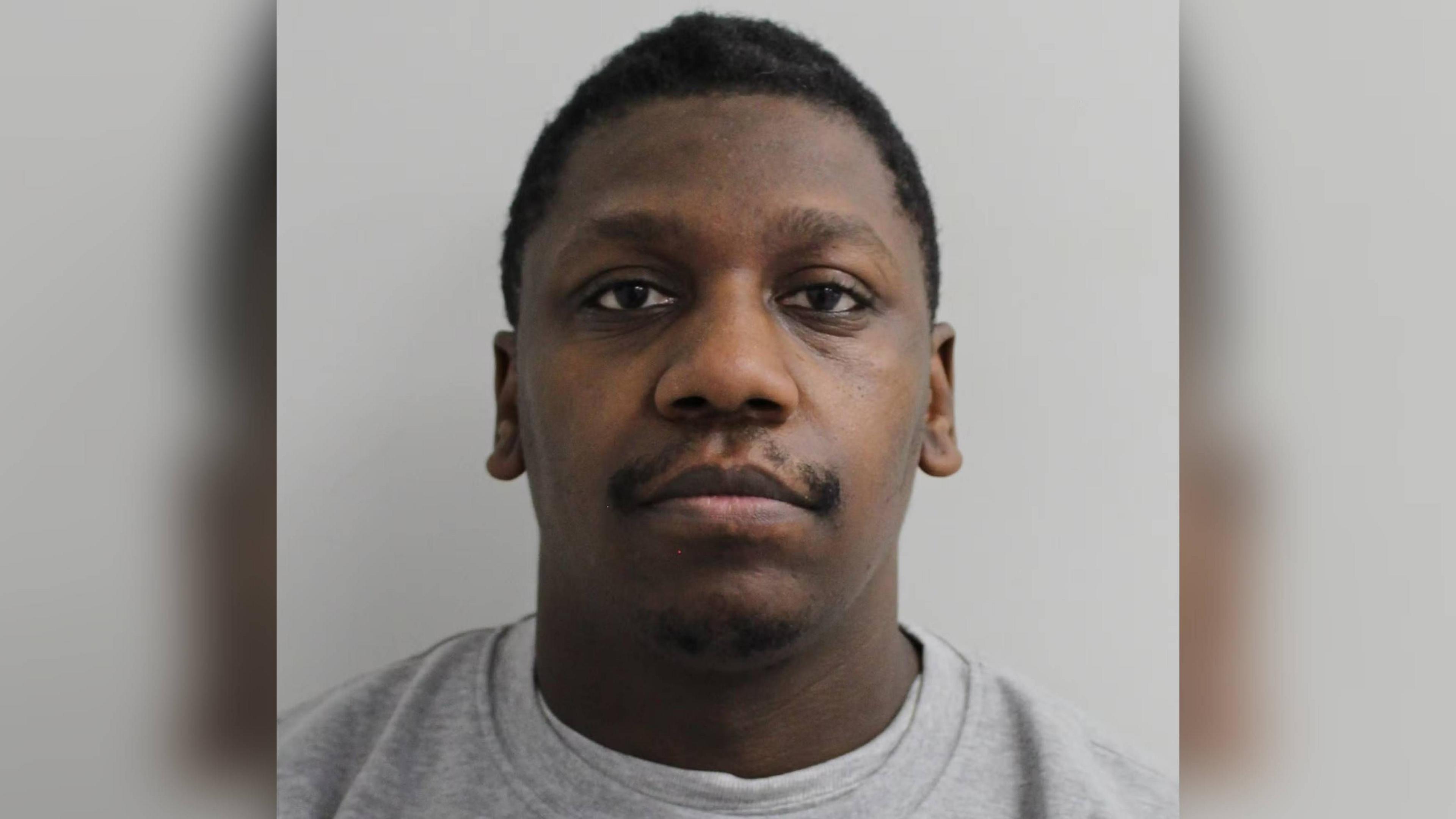 Jazz Reid, in a police custody shot, looking straight at the camera, wearing a light grey top