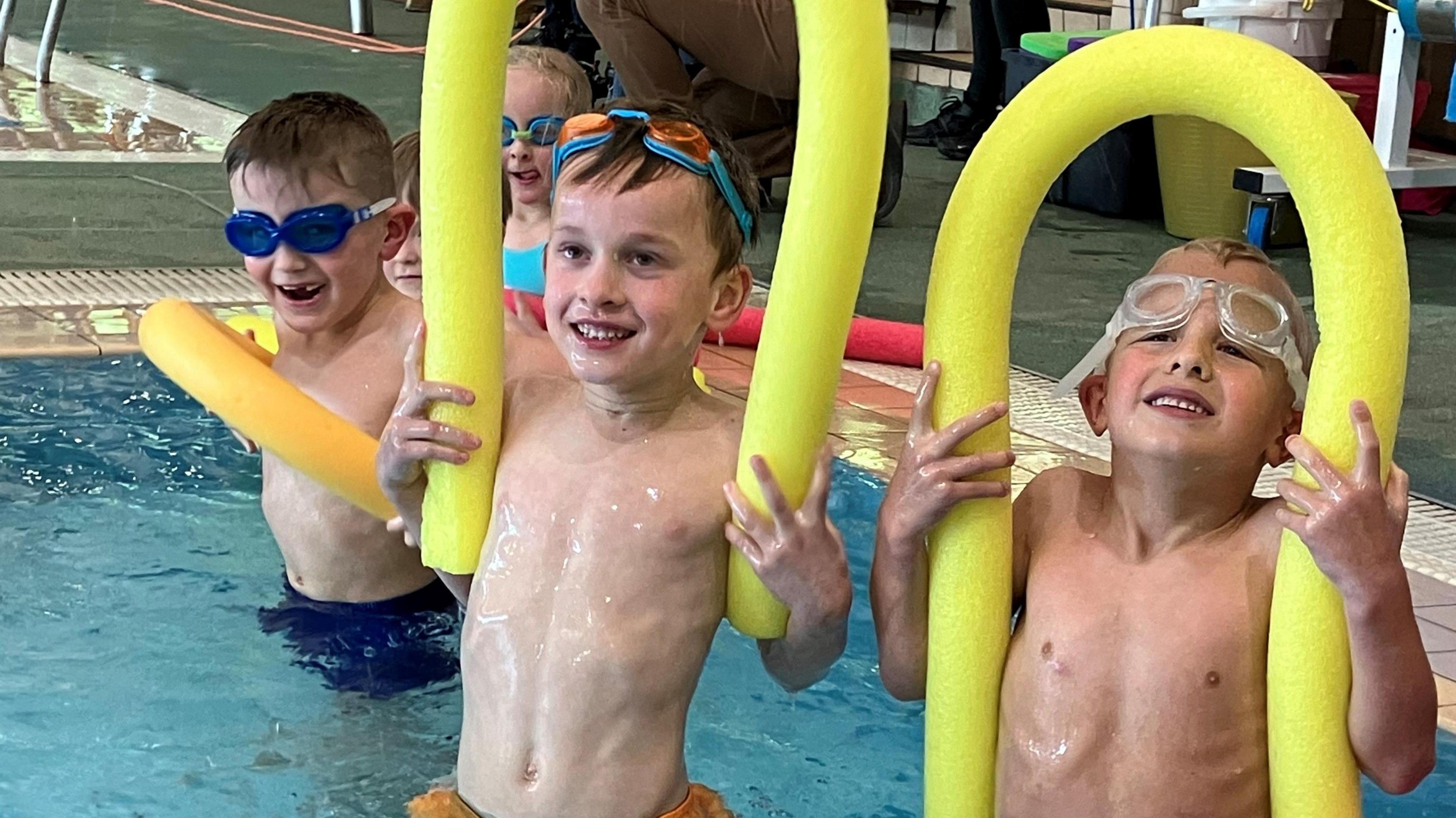 Children holding noodles in pool 