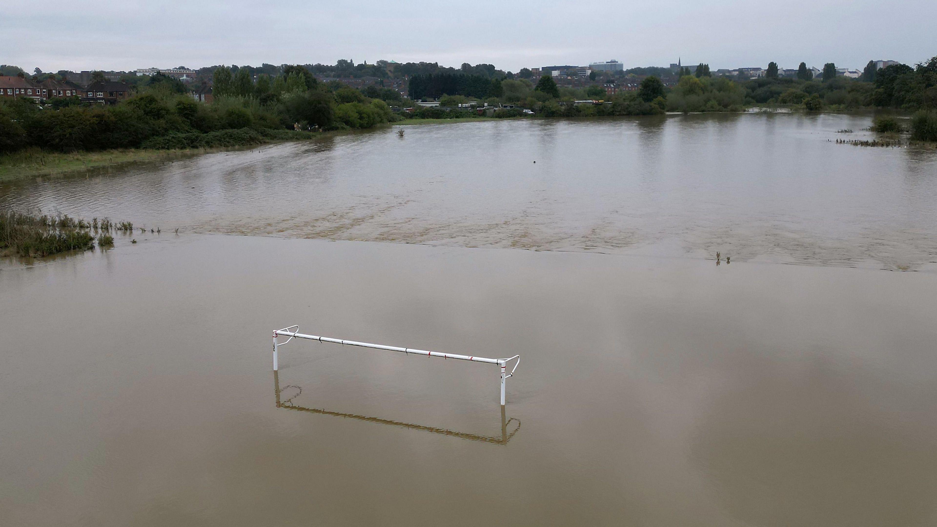 A football pitch in Northampton completely flooded. You can see half of the goal posts sticking out of the water.