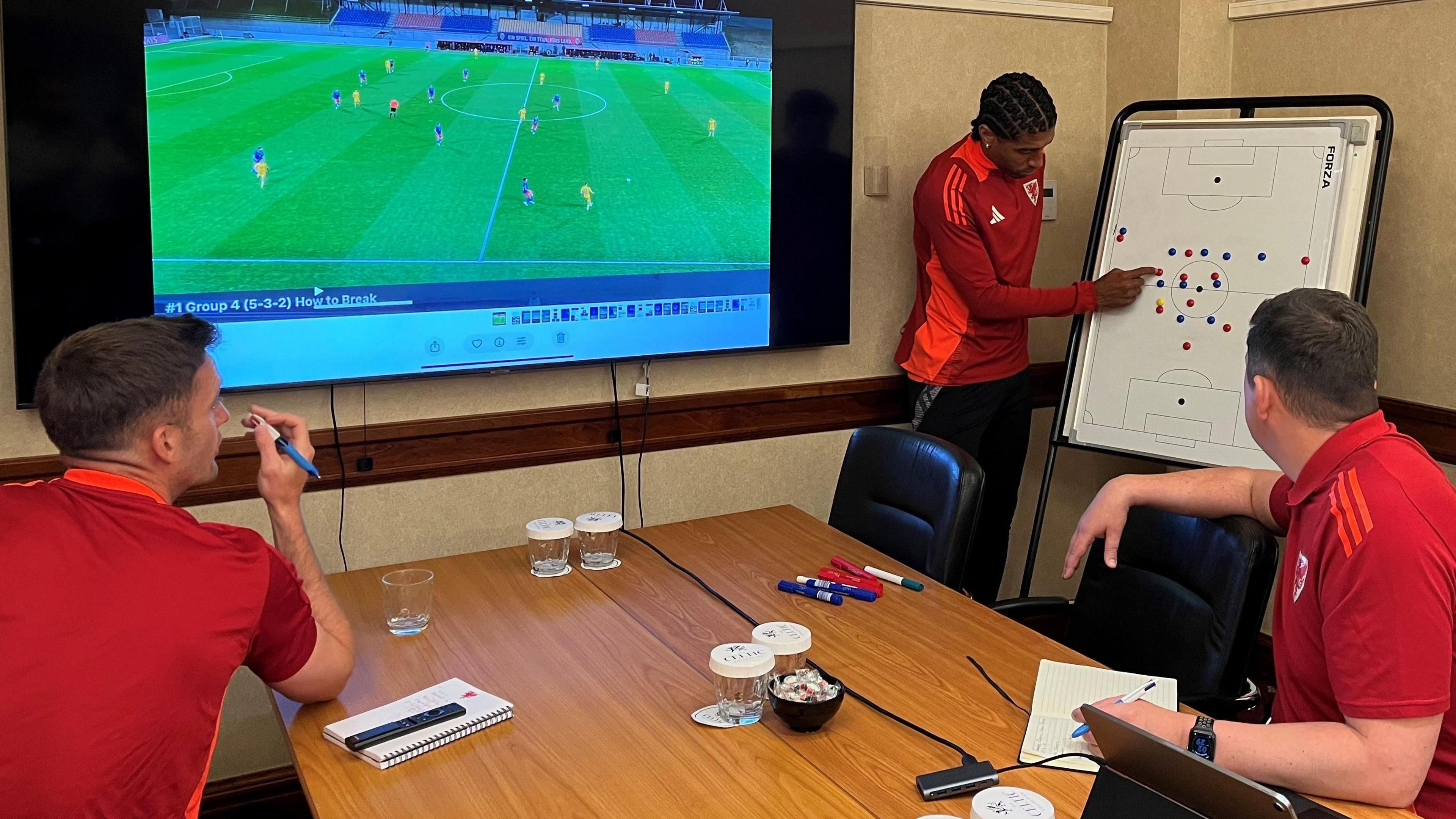 Dante (centre) points to a whiteboard as Richard Davies (right) and former Wales and Leicester midfielder Andy King (left) sit at a table watching