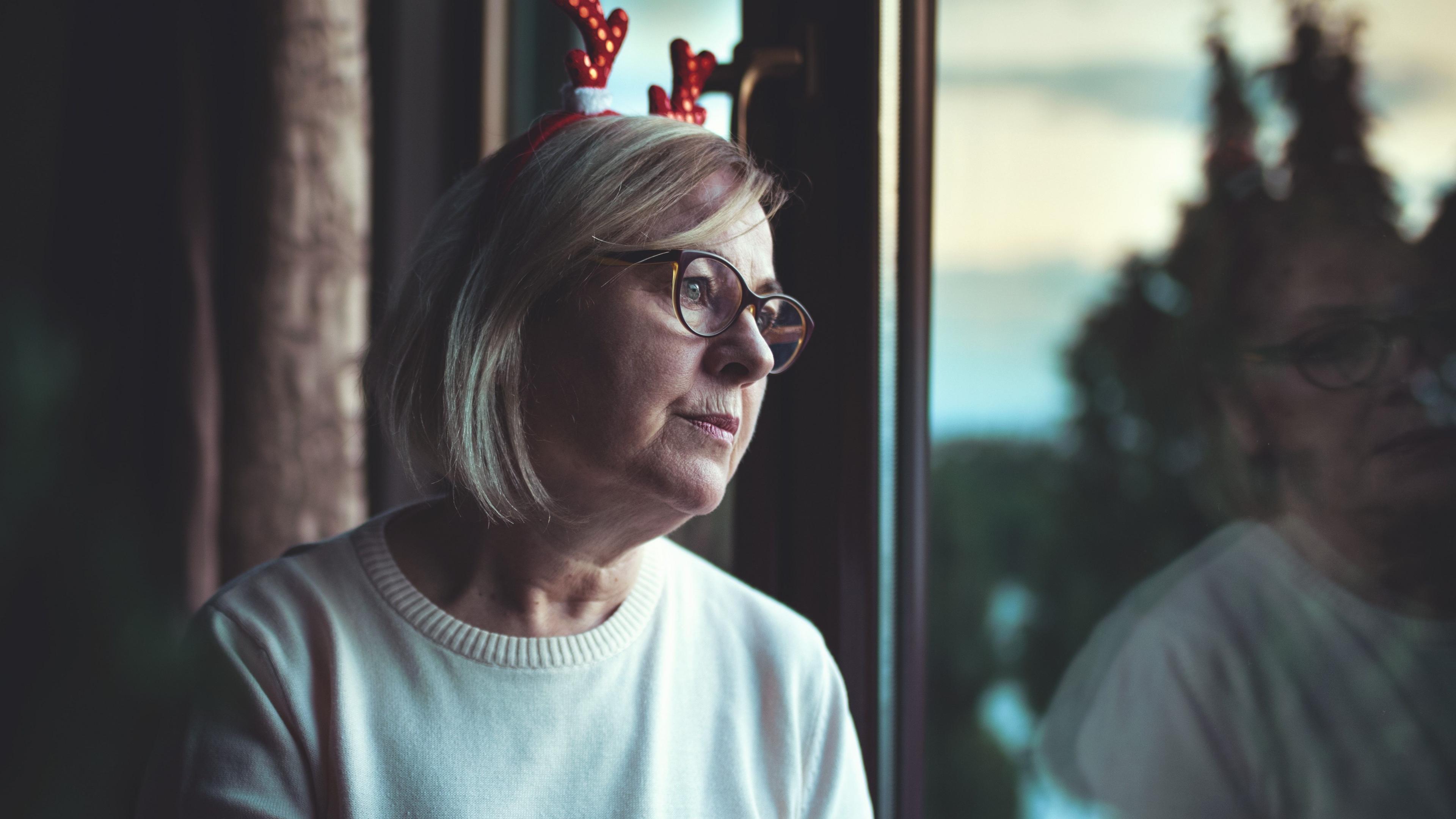 Woman wearing sparkly red Christmas antlers sitting alone and looking out of a window