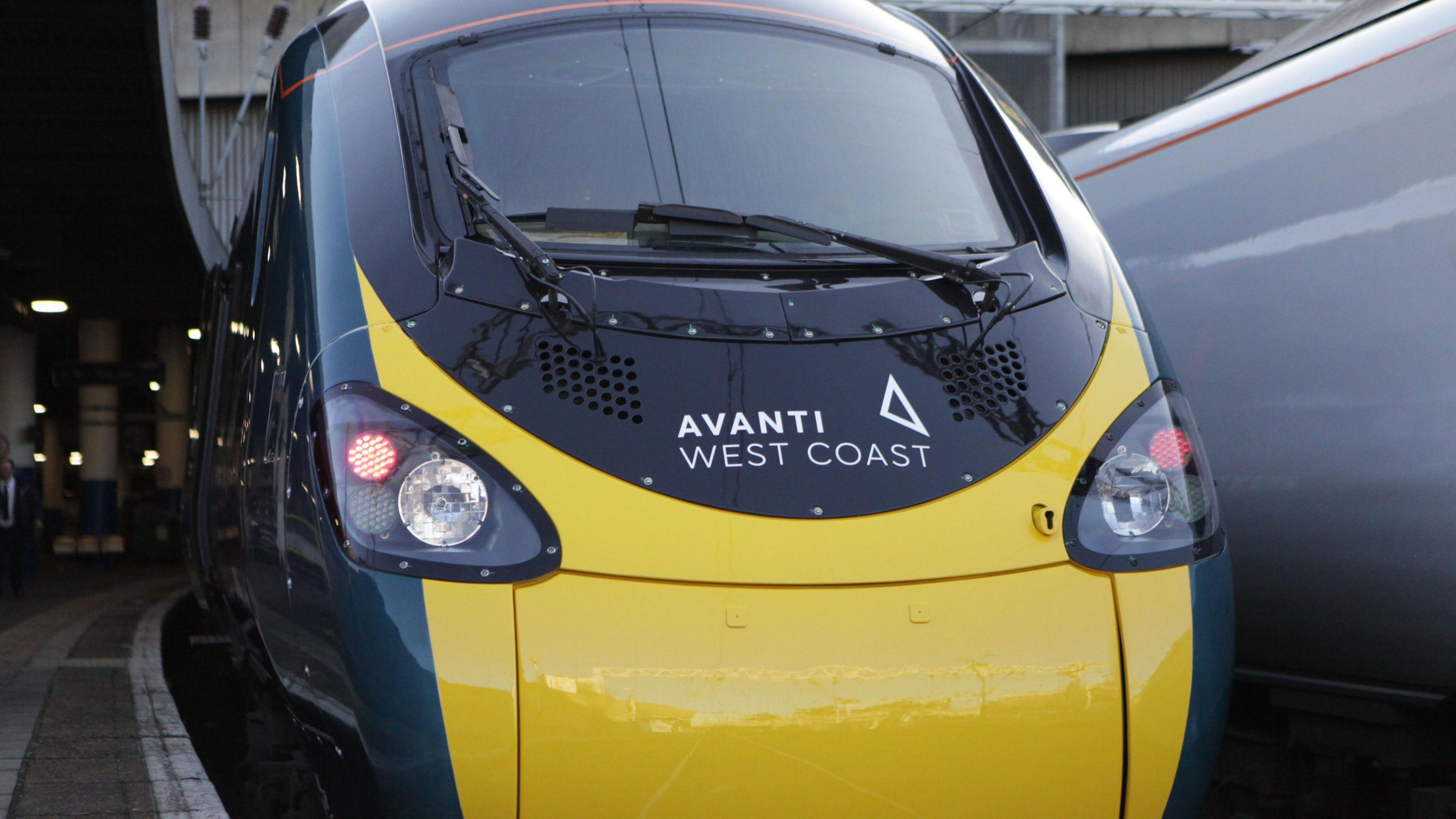 An Avanti West Coast train at Birmingham New Street. The train is yellow on the front with dark green patches down the side.