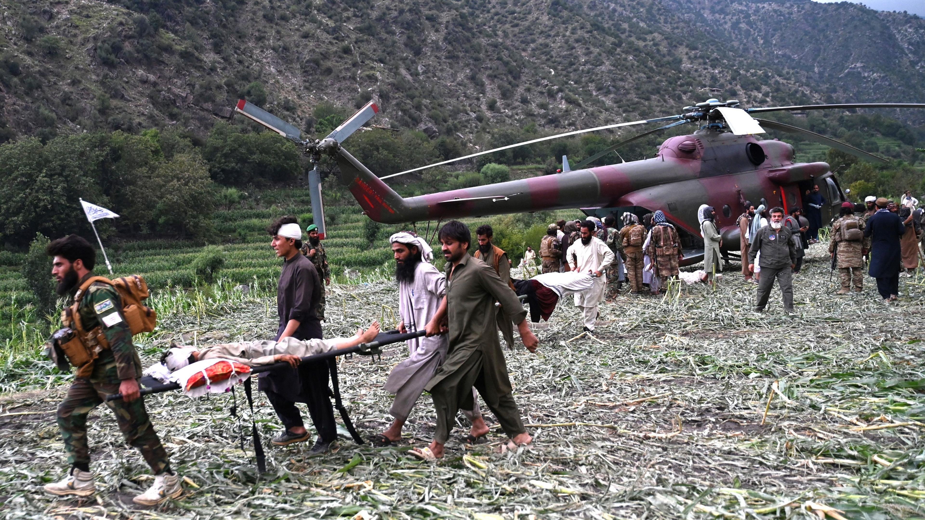 Afghan volunteers and Taliban move injured people near a military helicopter