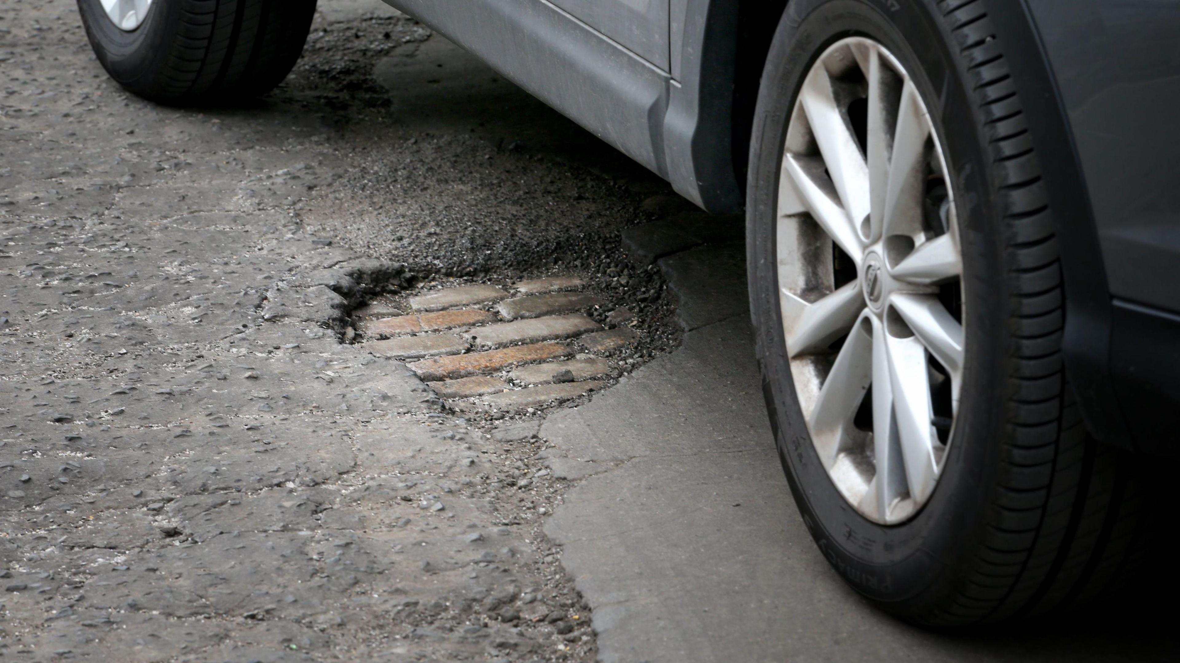 A car driving across a pothole, which is visible in the centre of the photo.