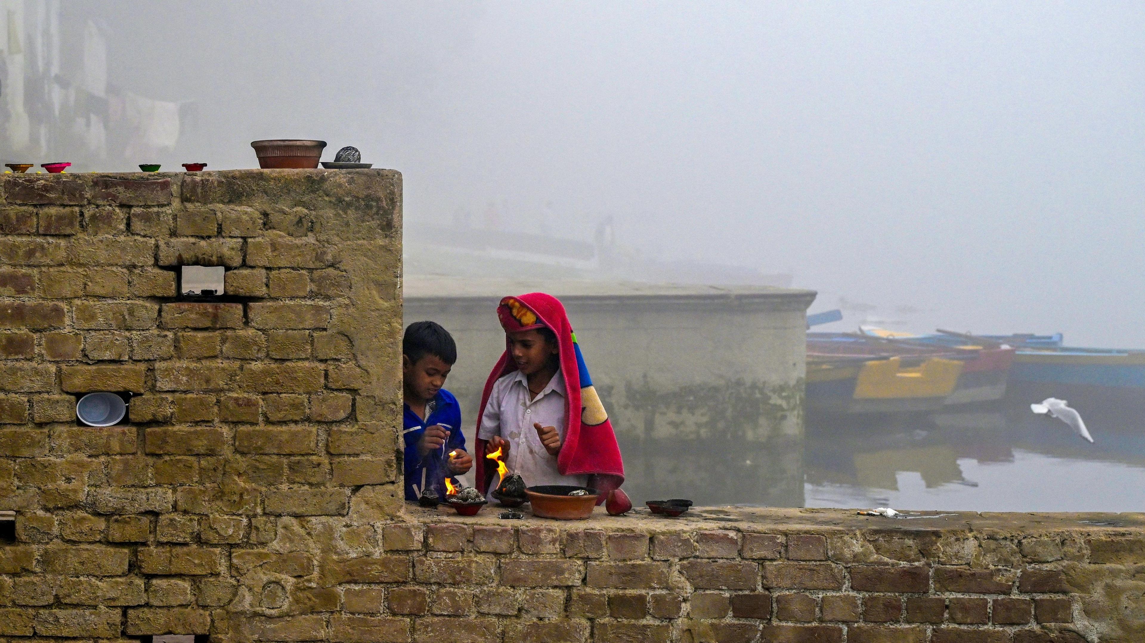 Boys light lamps on a brick wall on a bank of the river Yamuna in Delhi. Smog engulfs their surroundings