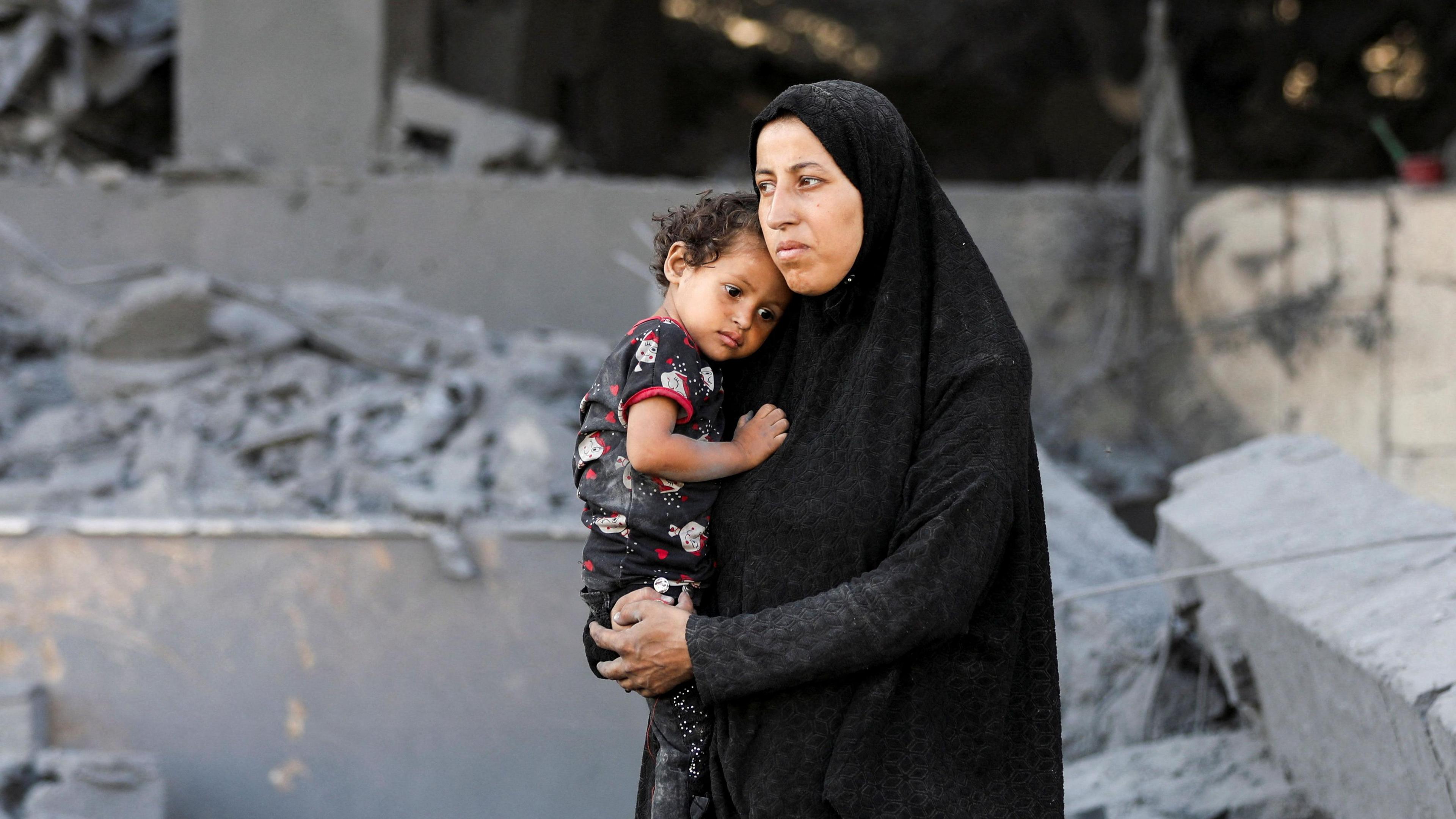 A Palestinian woman looks on holding a child at the site surrounding an evacuated UNRWA clinic where displaced people were taking shelter, following an overnight Israeli strike, in Gaza City on 6 August 2025.