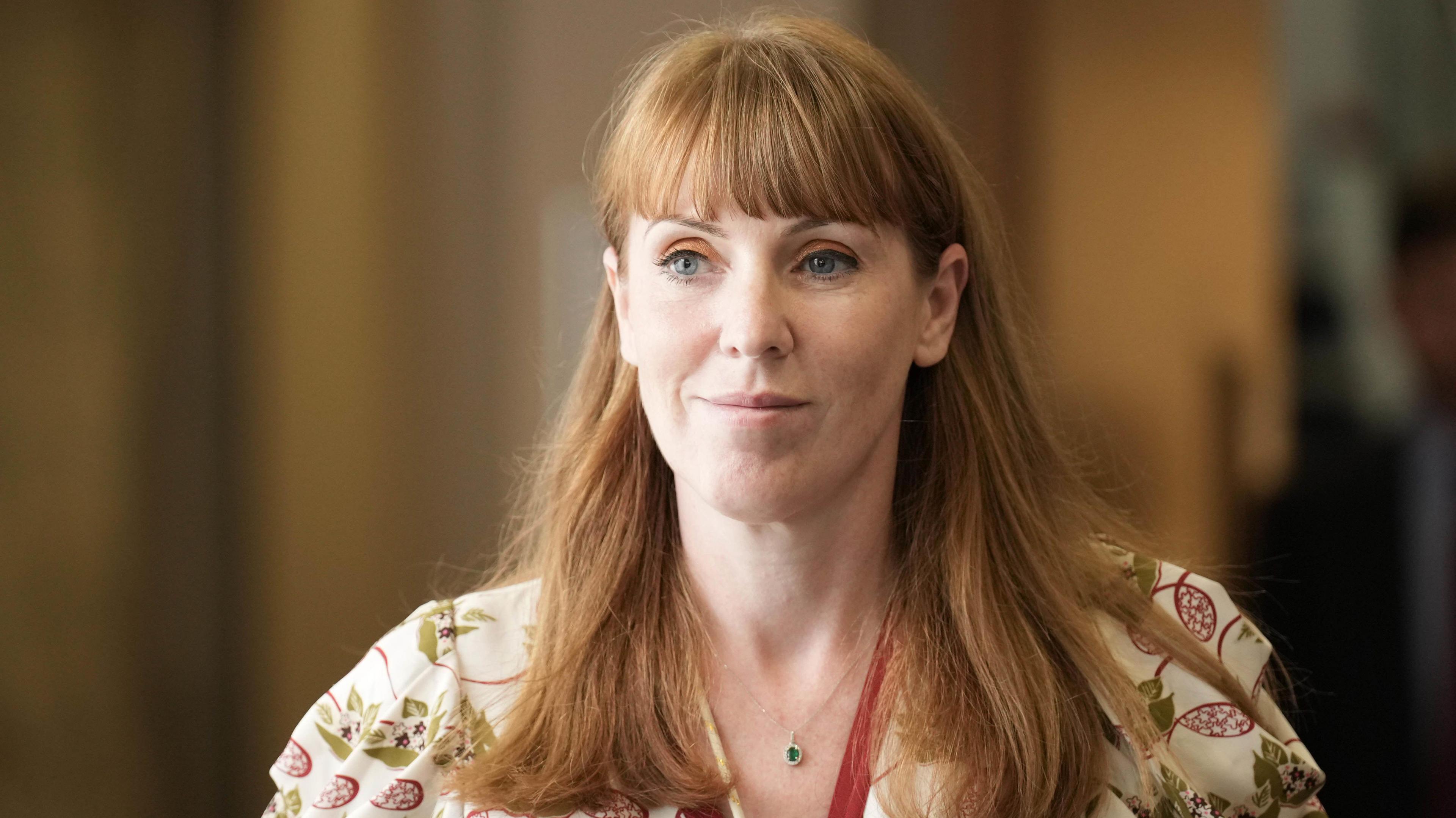 Deputy Prime Minister Angela Rayner looking into the distance in a hallway wearing a white dress with green and red patterns on it