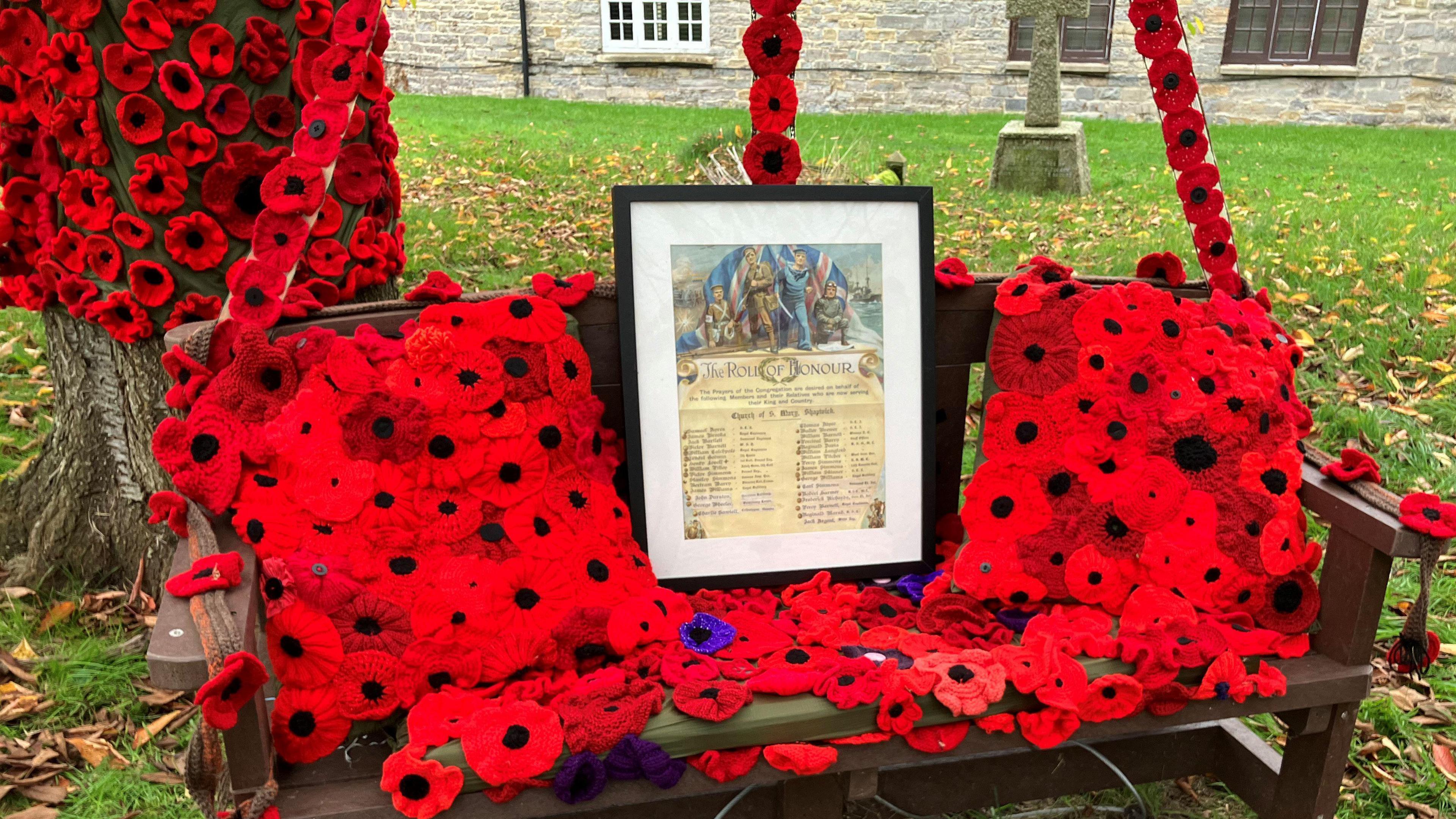 Brown bench that is covered in red crocheted Remembrance poppies