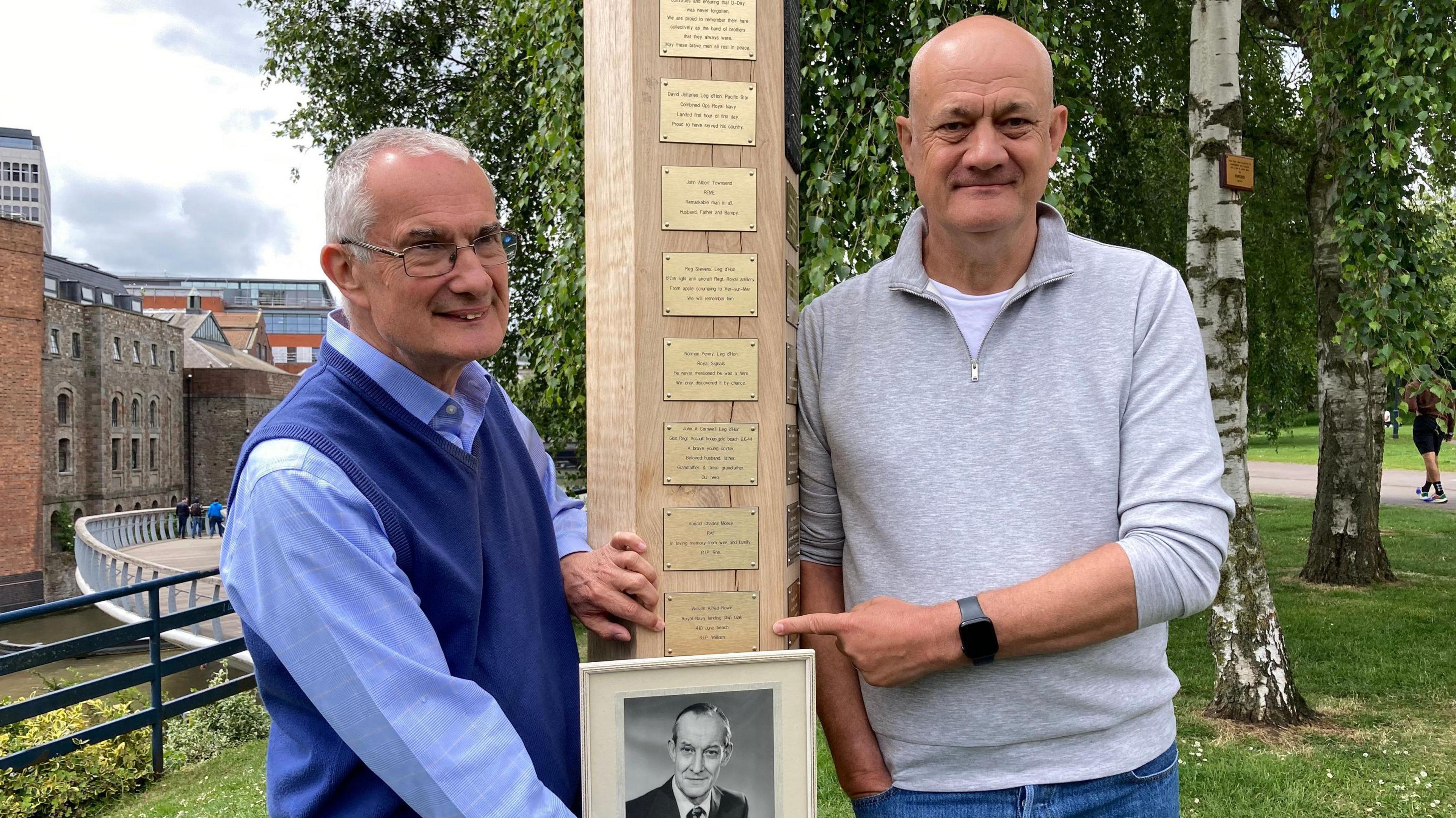 Philip and Peter Rowe holding a framed photo of their father at the memorial. 