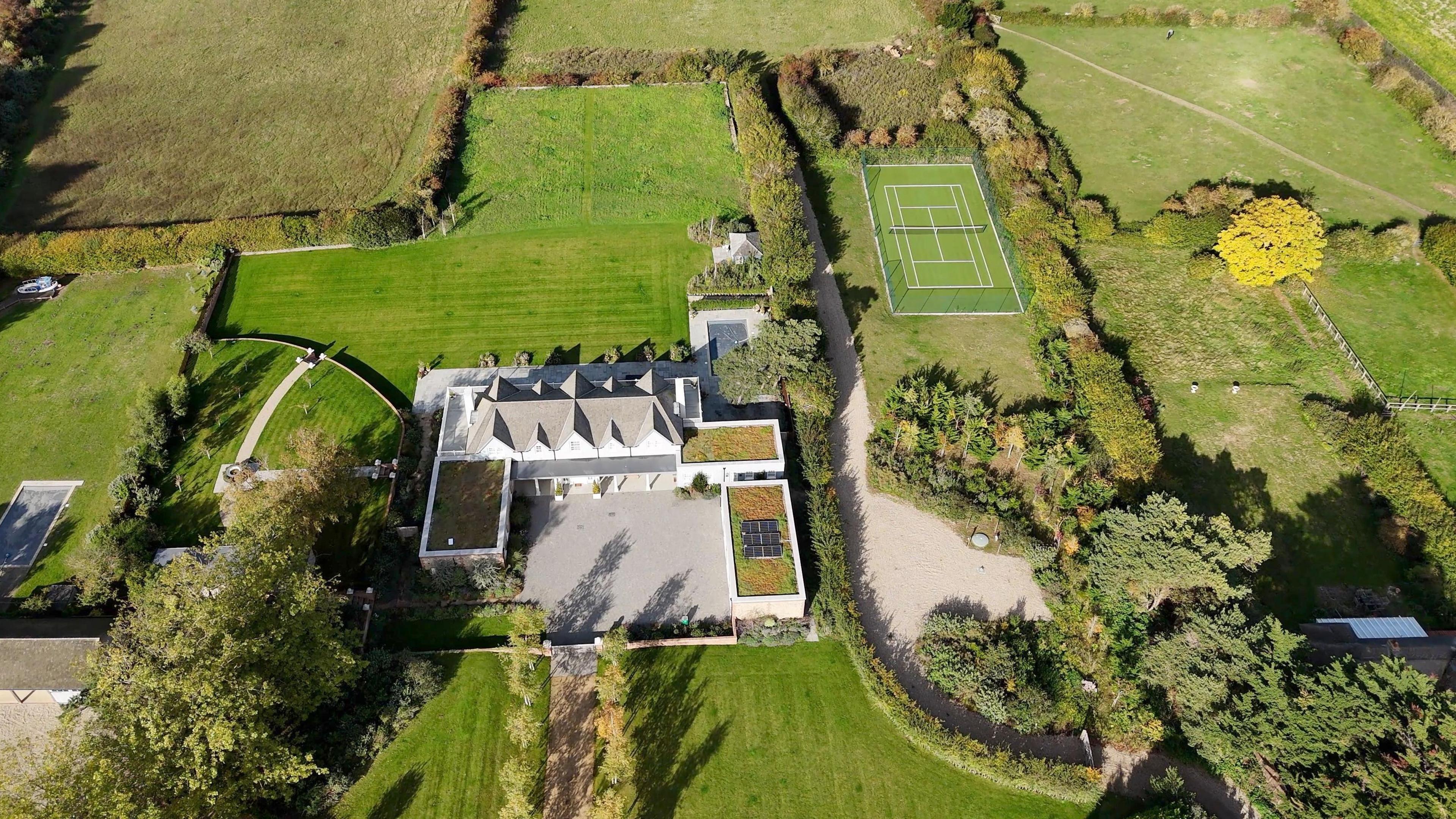 A drone image of Larkfield in Blakeney, showing the house, extensions, tennis court, swimming pool and lawns and wild grasslands around.