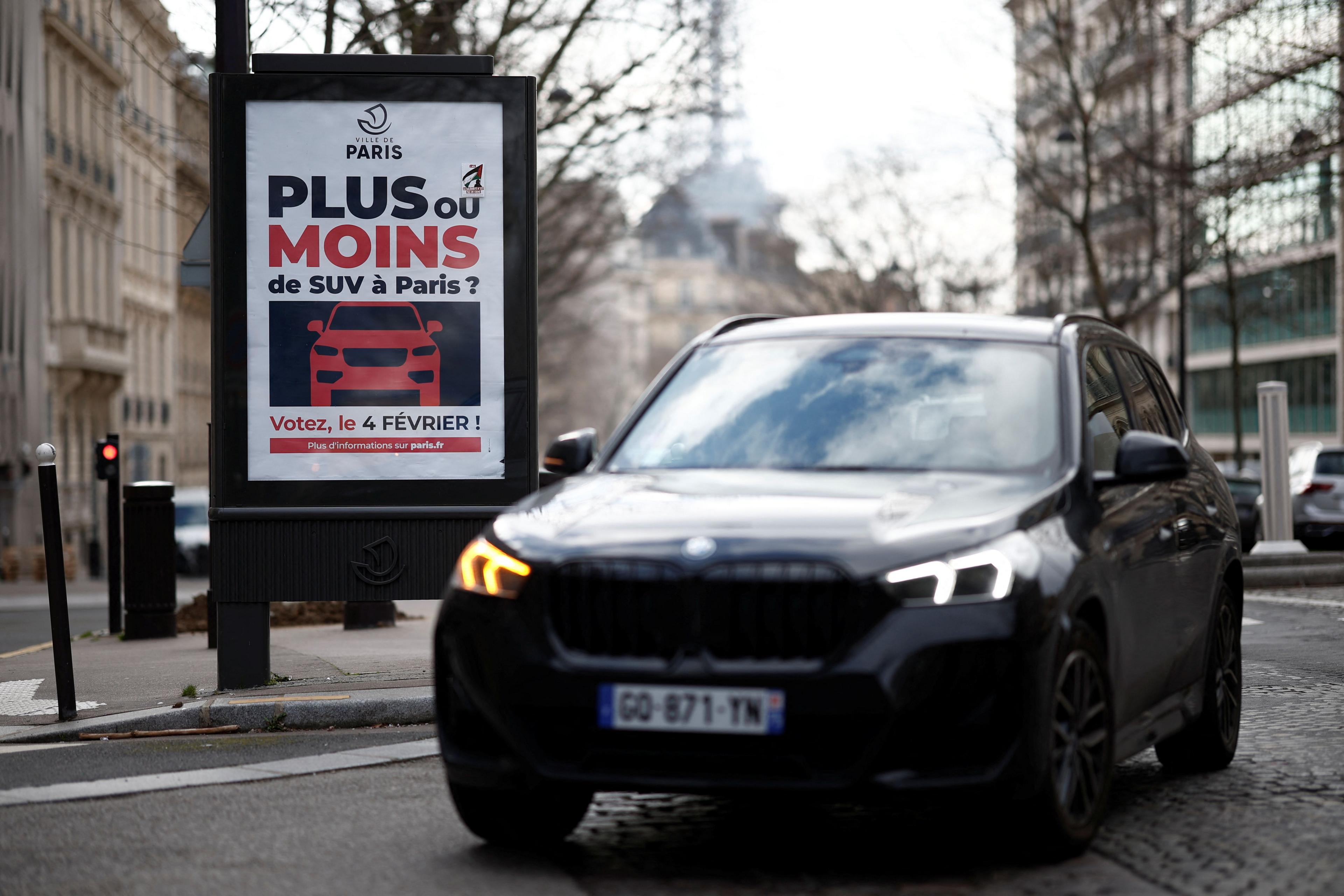 An SUV drives past a poster in Paris publicising a vote in 2024 over raising parking fees to reduce emissions and increase pedestrian safety