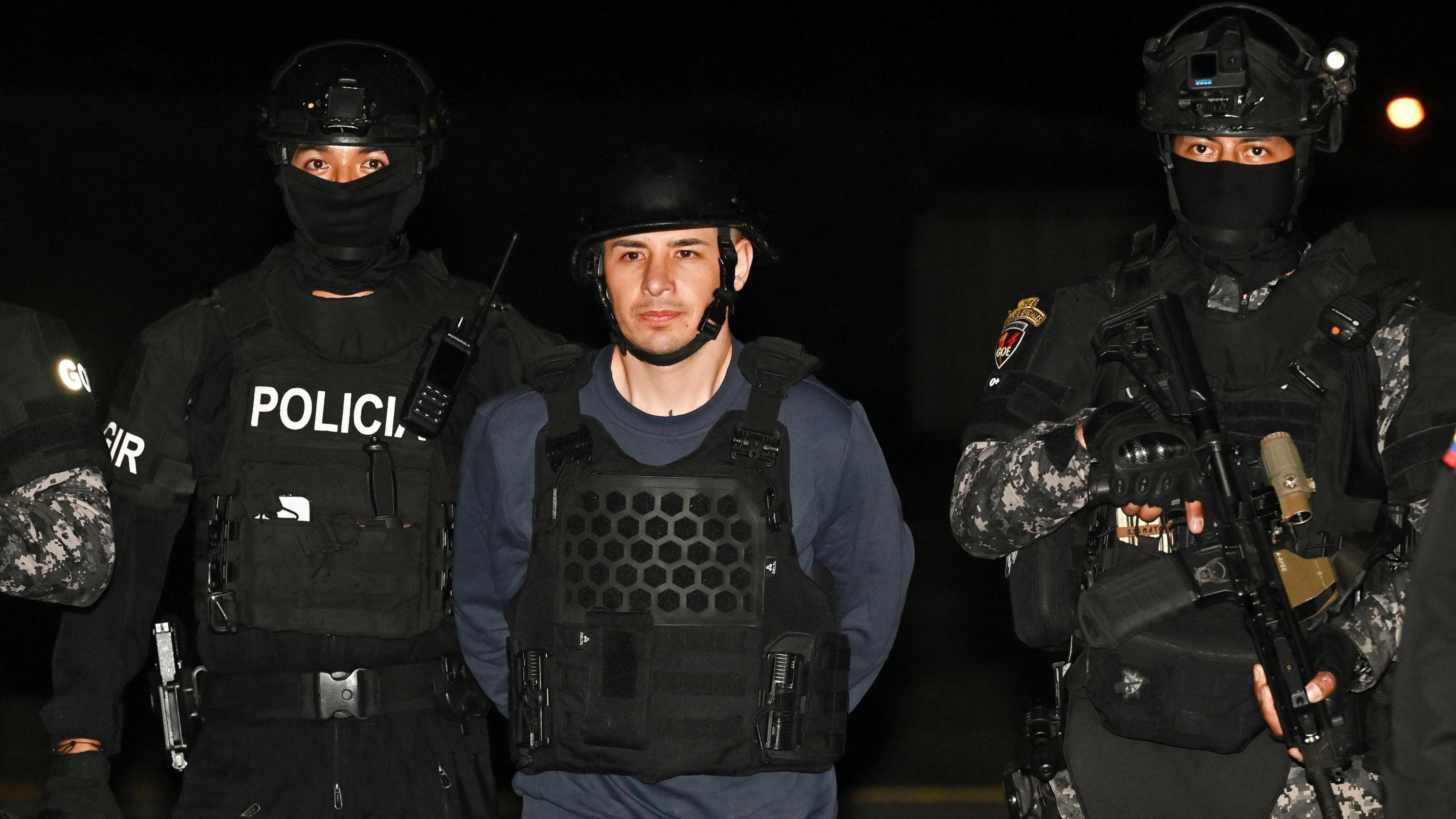 Ecuadorean police escort Ángel Esteban Aguilar in the cover of darkness. All wear tactical gear.