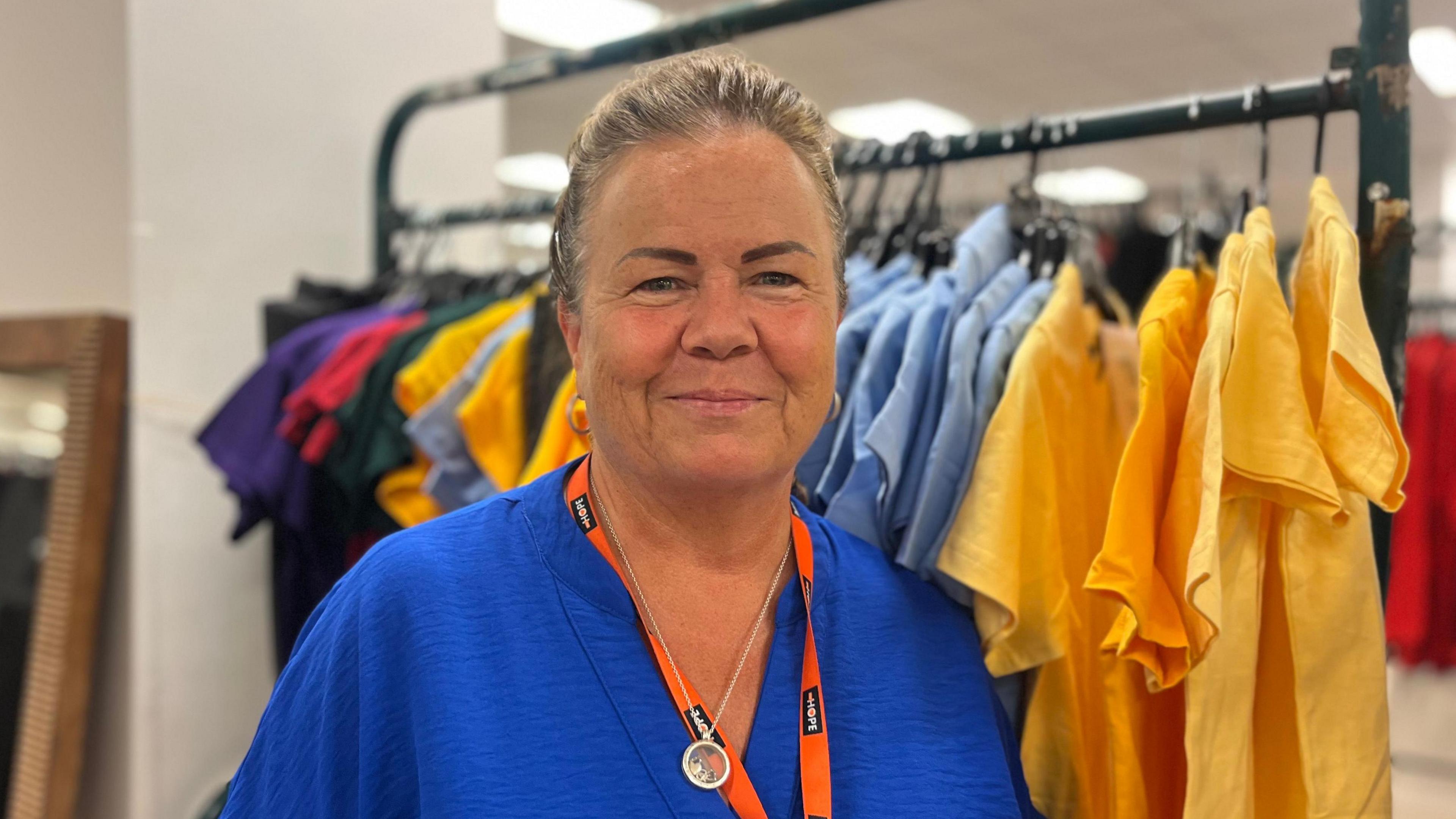 Louise Atherton has brown greying hair and is in a blue top in front of a rail school uniform shirts