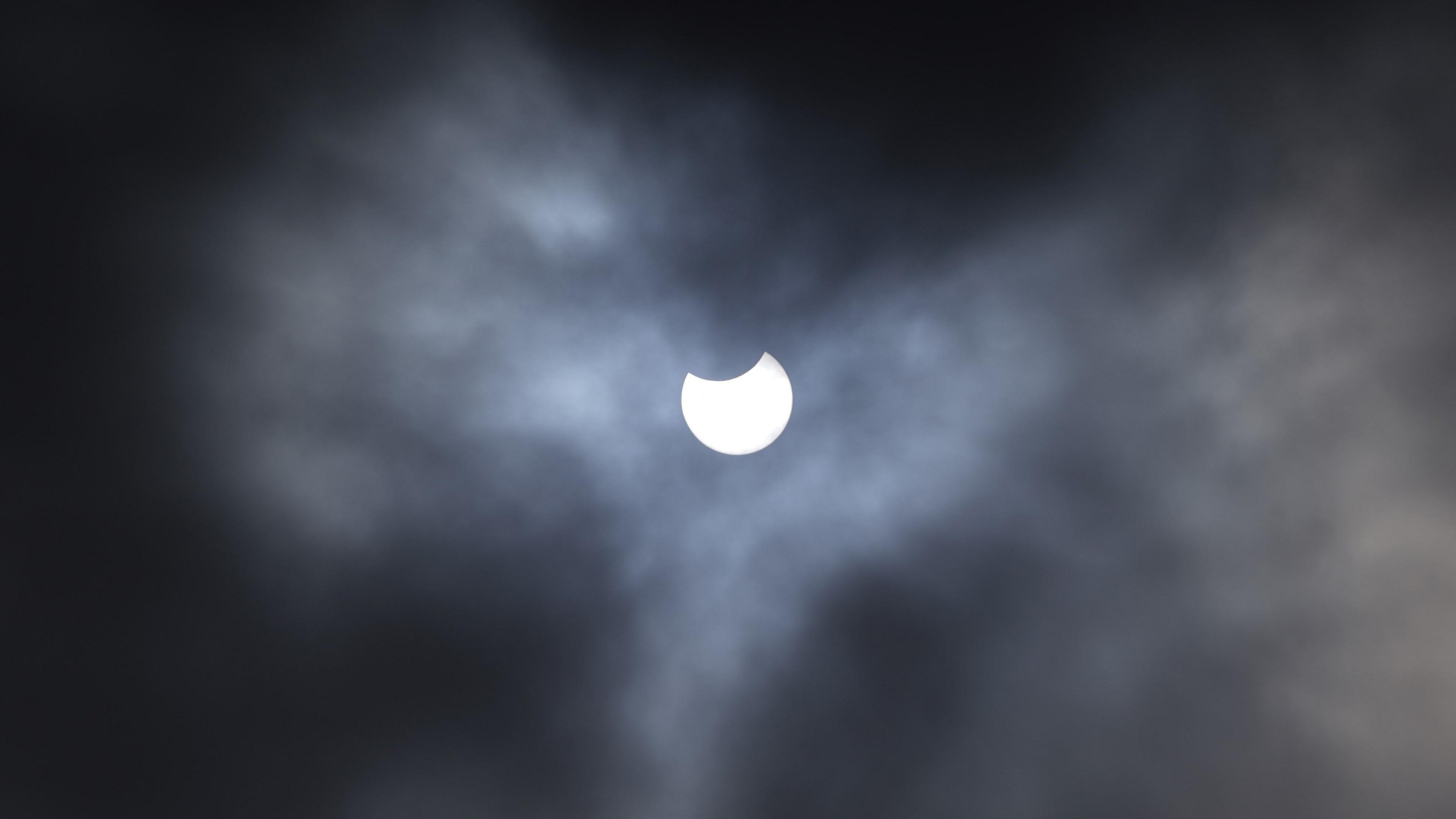 White Moon in a dark, partially cloudy sky with what looks like a bite taken out of the top