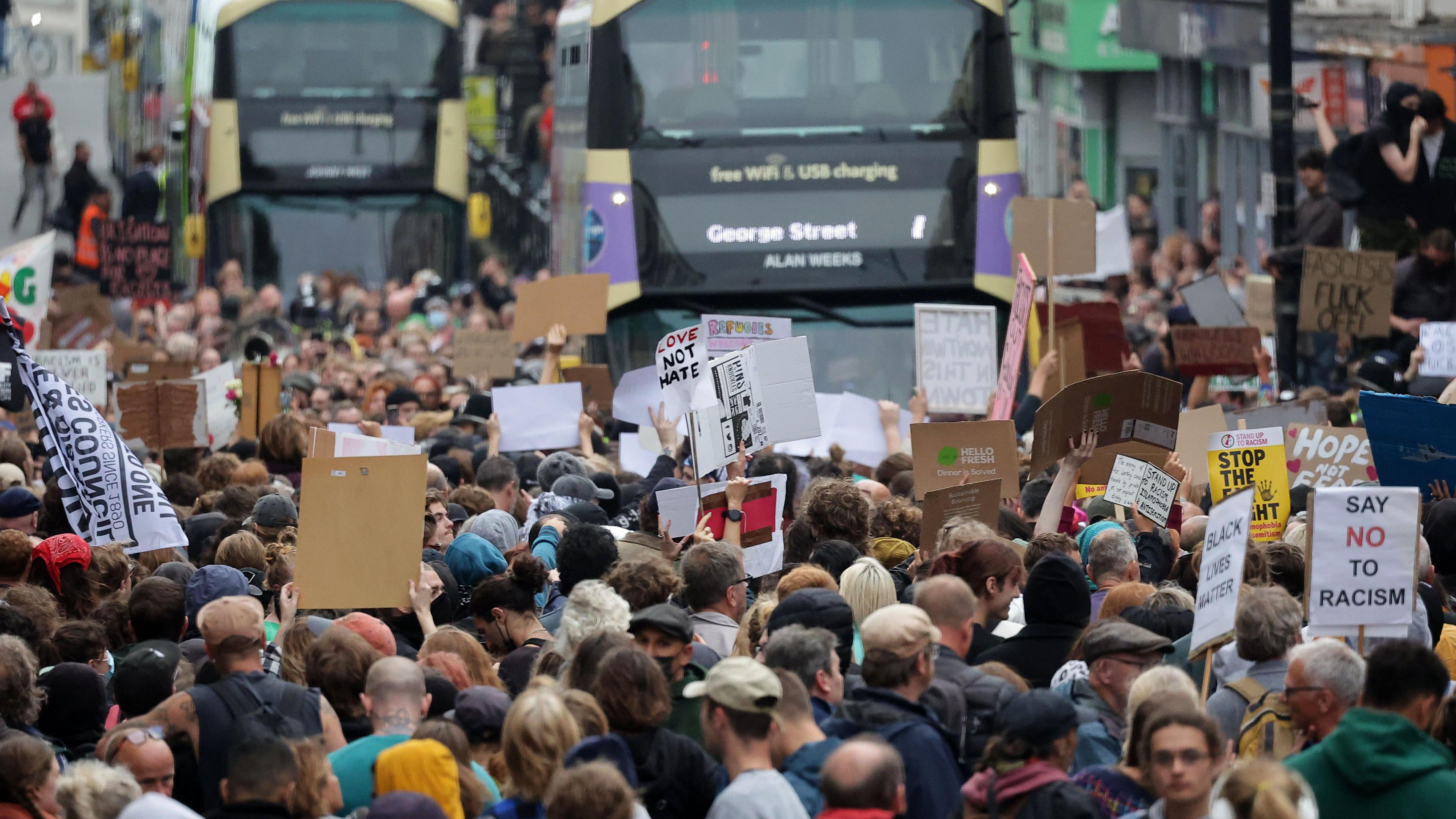 Anti-racism demonstrators hold placards as two buses are held up on Queens Road