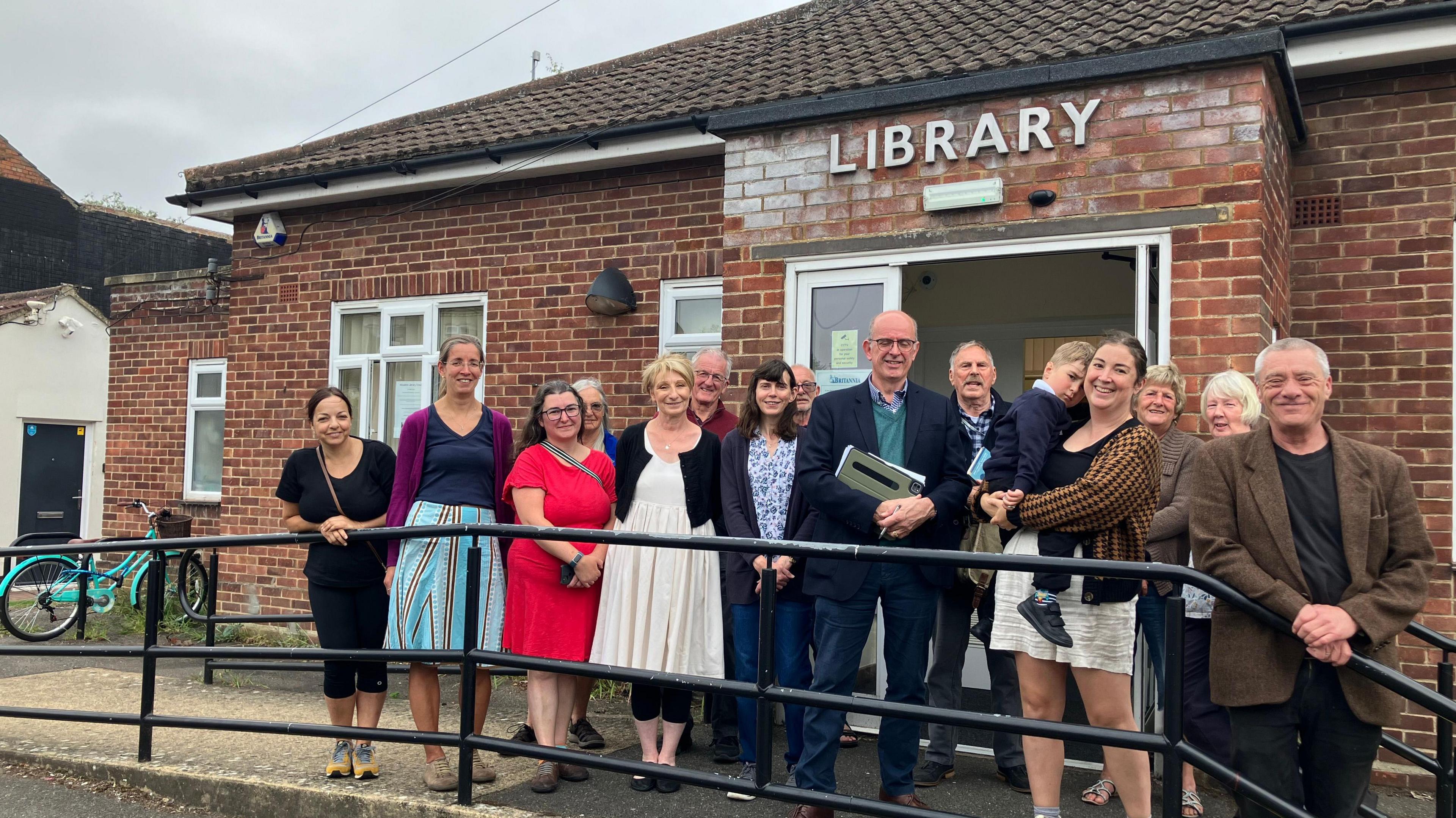 Supporters of Woodston Library standing in front of the small red brick building in Peterborough 