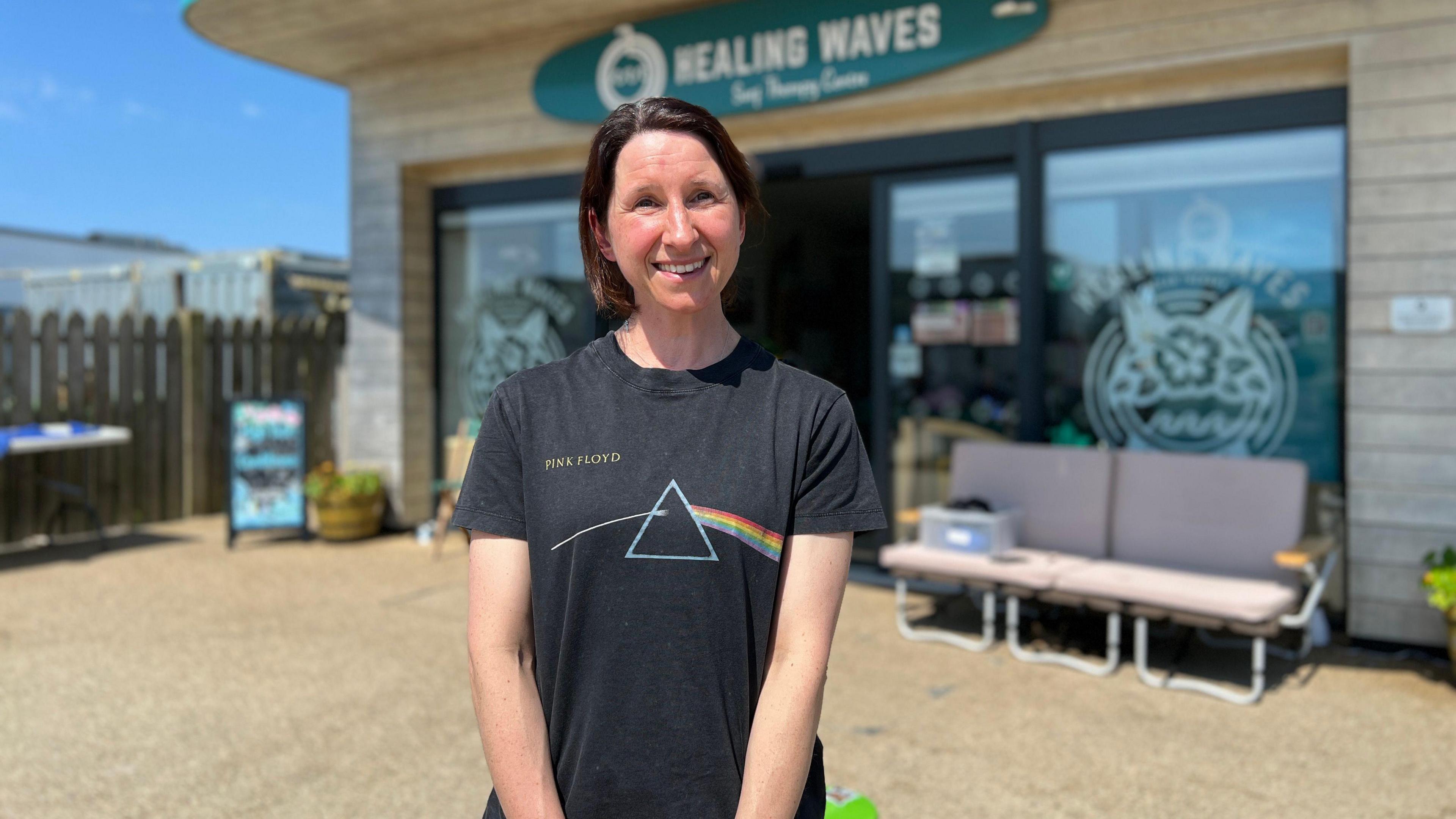 Lynne smiles at the camera as she stands in front of the Healing Waves headquaters