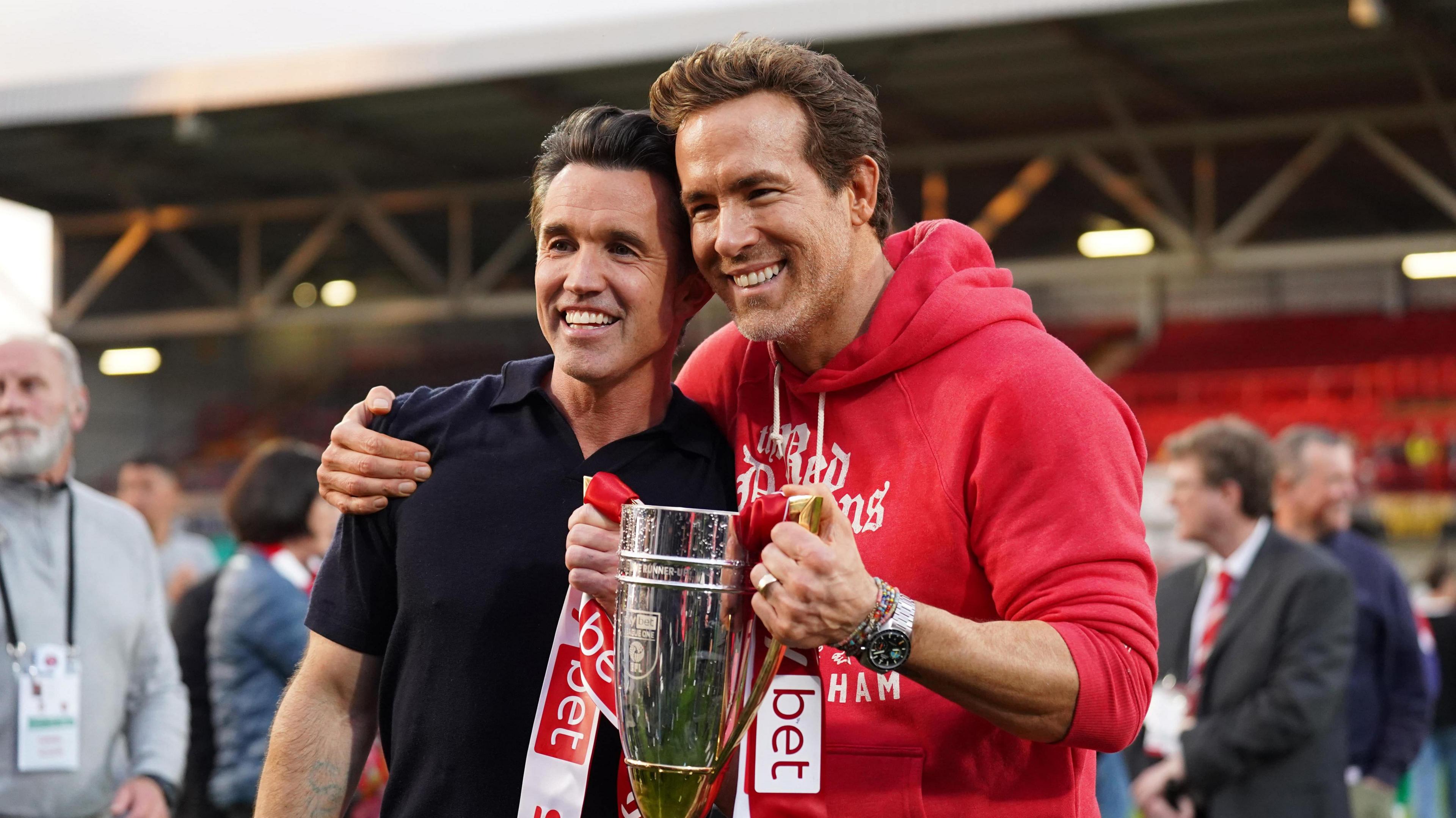 Ryan Reynolds and Rob McElhanney grin as they hold up the trophy following the club's promotion to the Sky Bet Championship