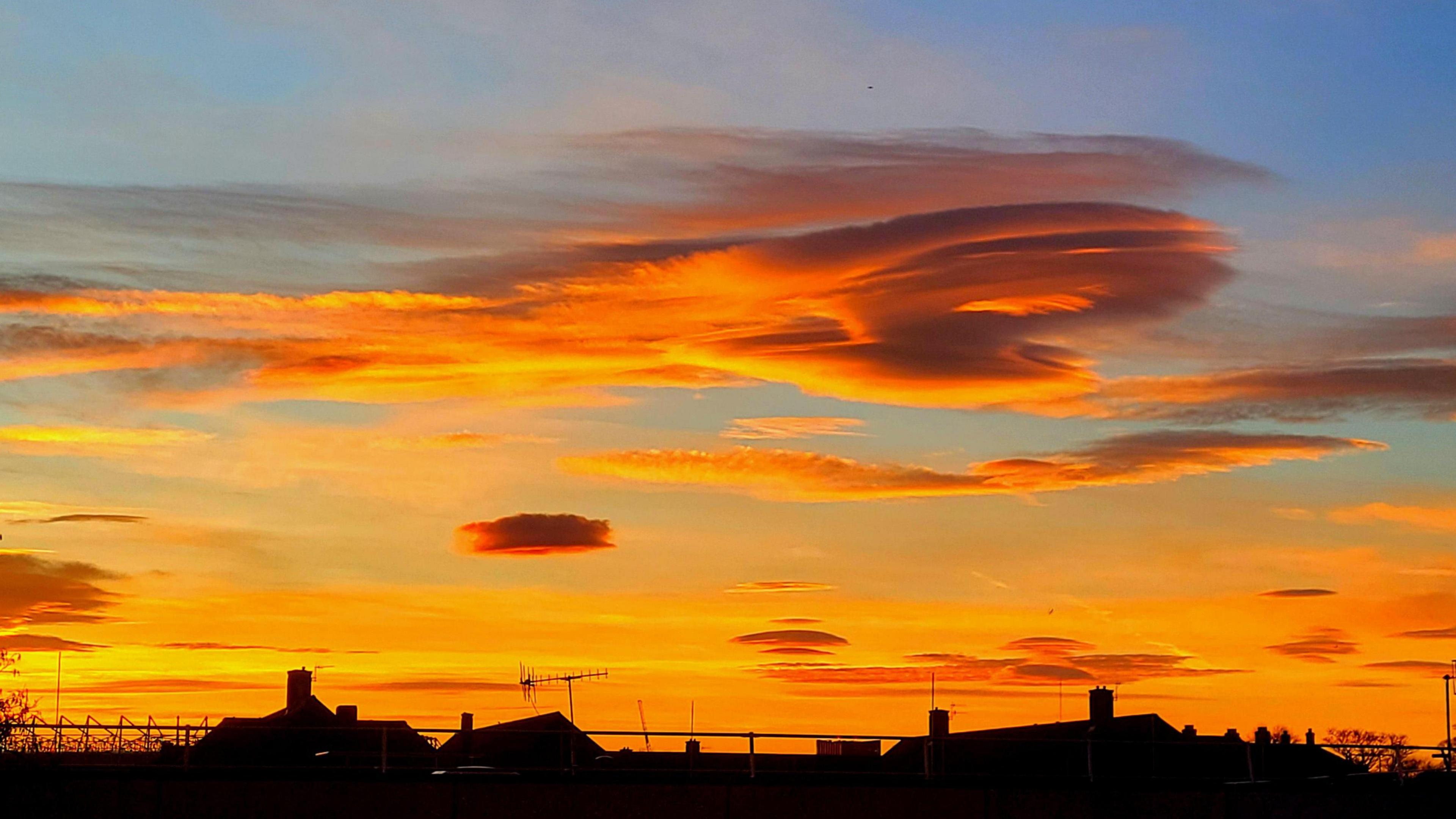 Layers of cloud in an orange sky above the silhouette of roof tops