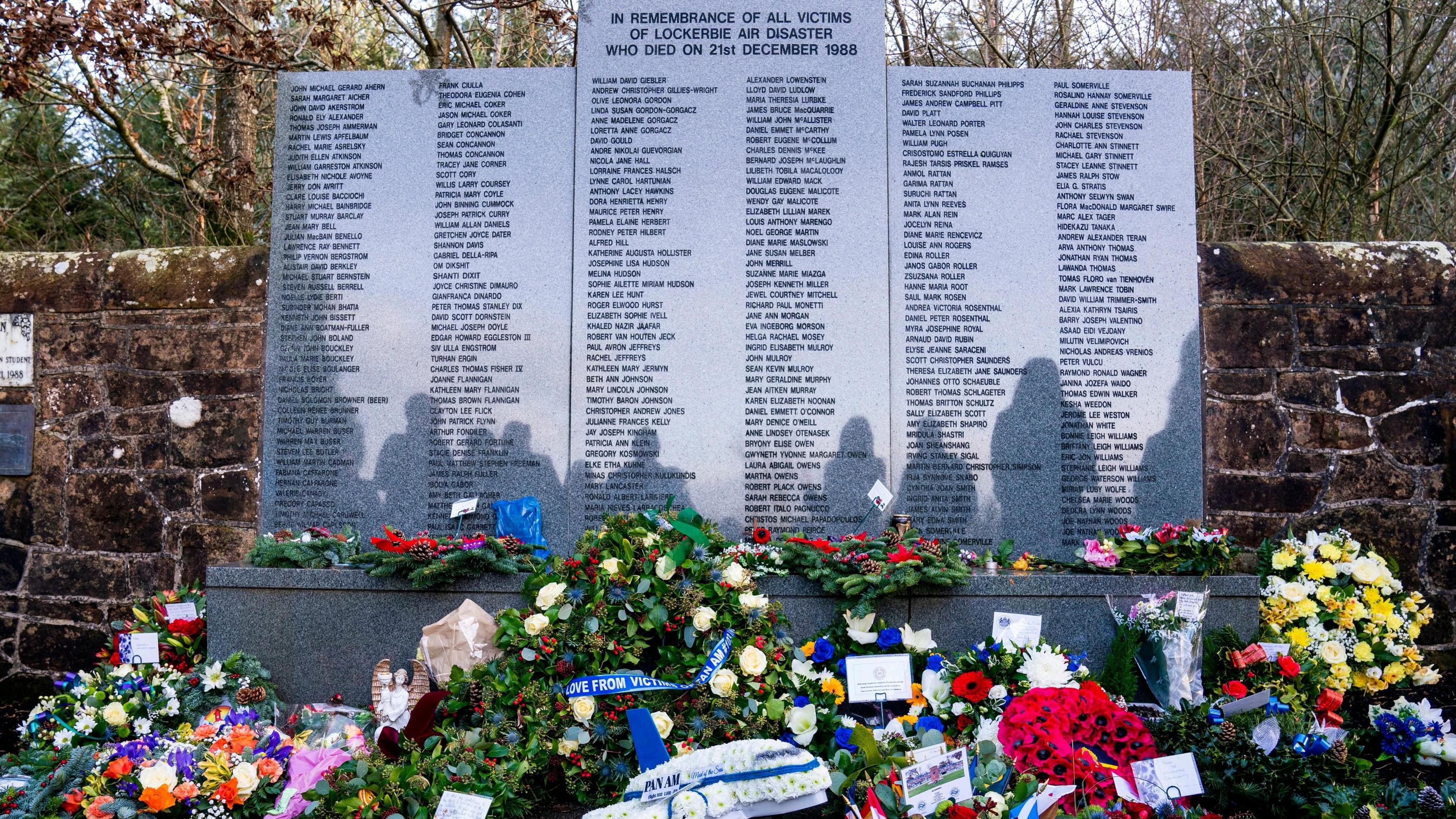 Wreaths and floral tributes in front of the Lockerbie bombing memorial, a large grey granite structure containing the names of the victims