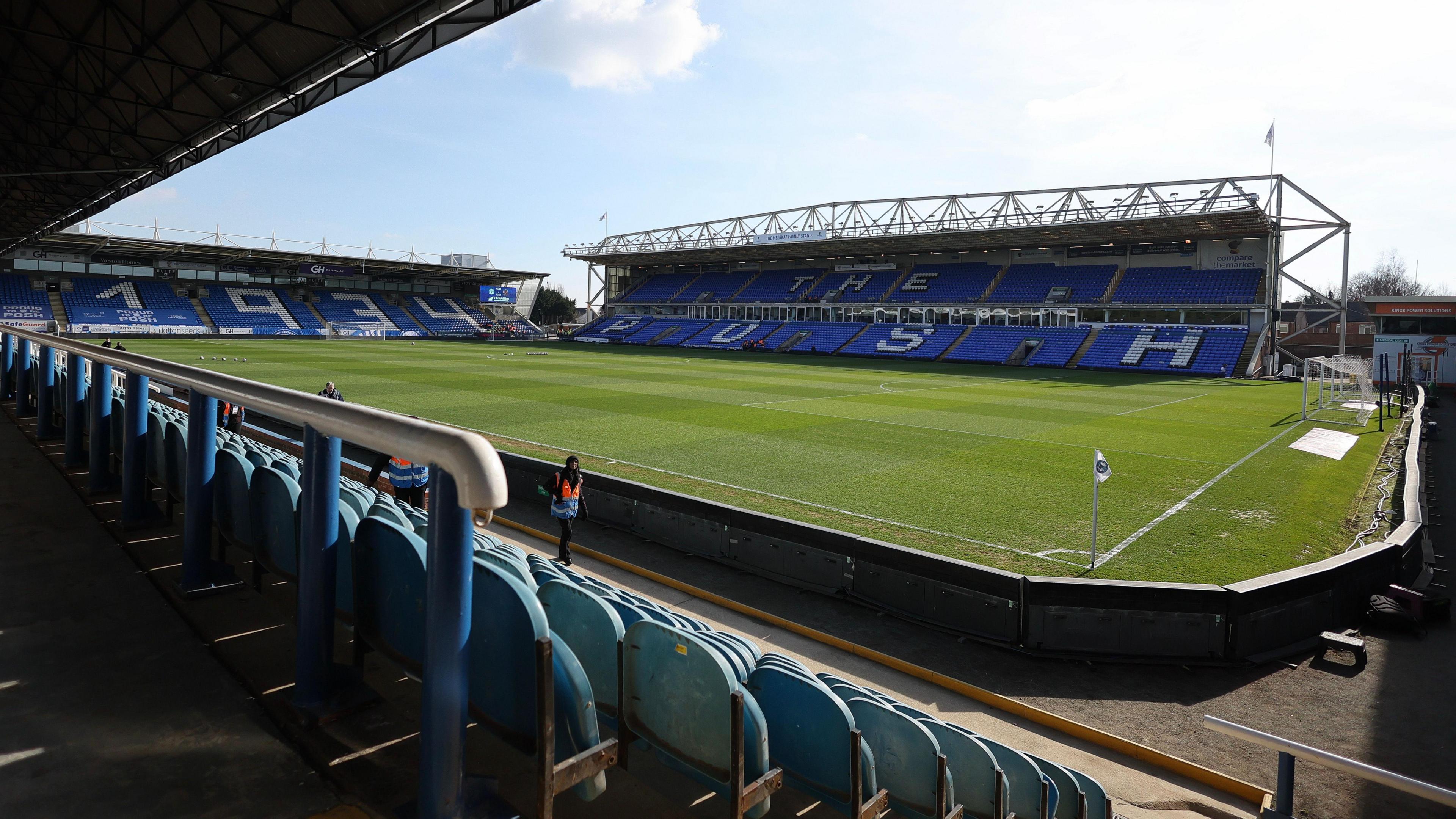 A wide angle shot of the inside of Peterborough United's Weston Homes stadium in London Road. There is a large green pitch and three of the stadium's stands, which have blue seats.