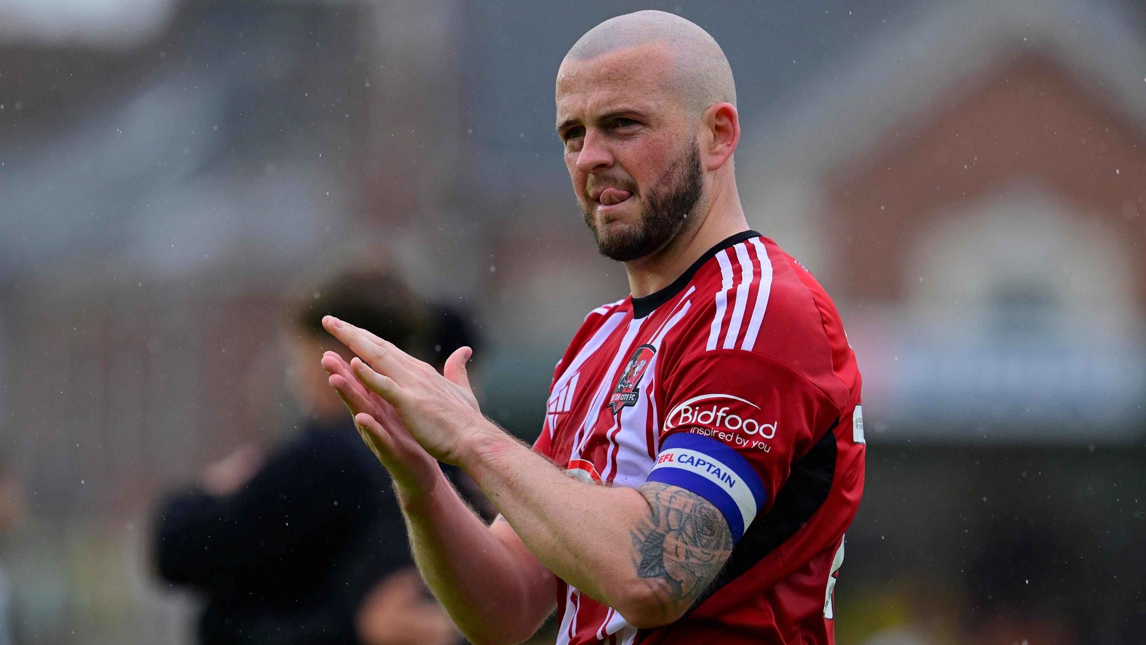 Pierce Sweeney clapping fans, wearing home Exeter City red and white stripes and the purple and white captain's armband