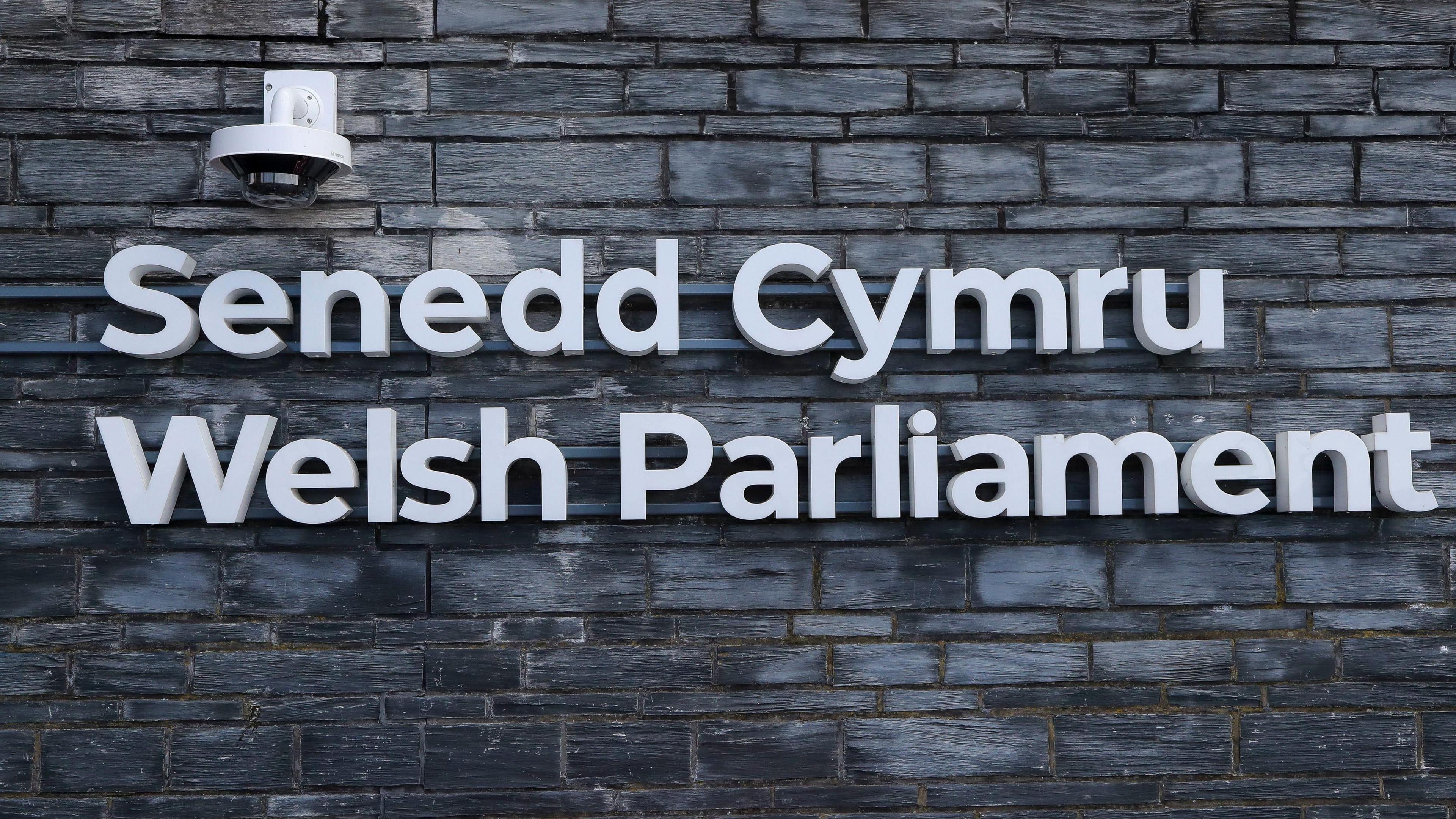 A picture of the Senedd Cymru/Welsh Parliament logo, spelt out in both languages, on a slate wall on the outside of the Senedd building in Cardiff Bay