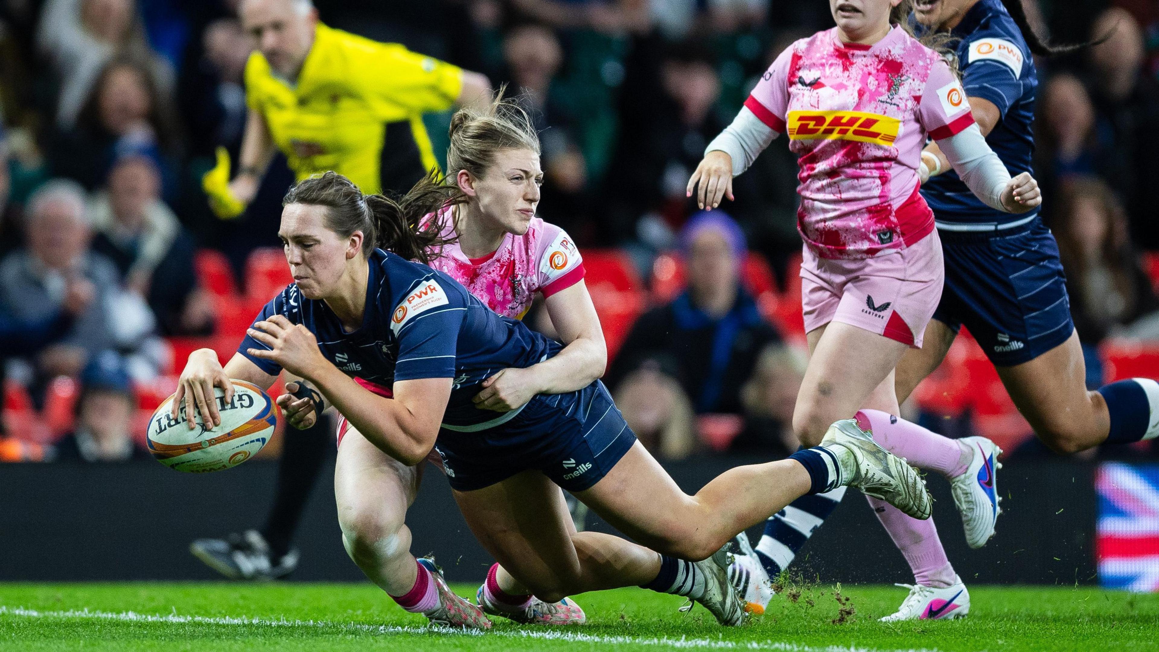 Emma Orr dives towards the line with the ball in her outstretched right arm under a tackle from a Harlequins player