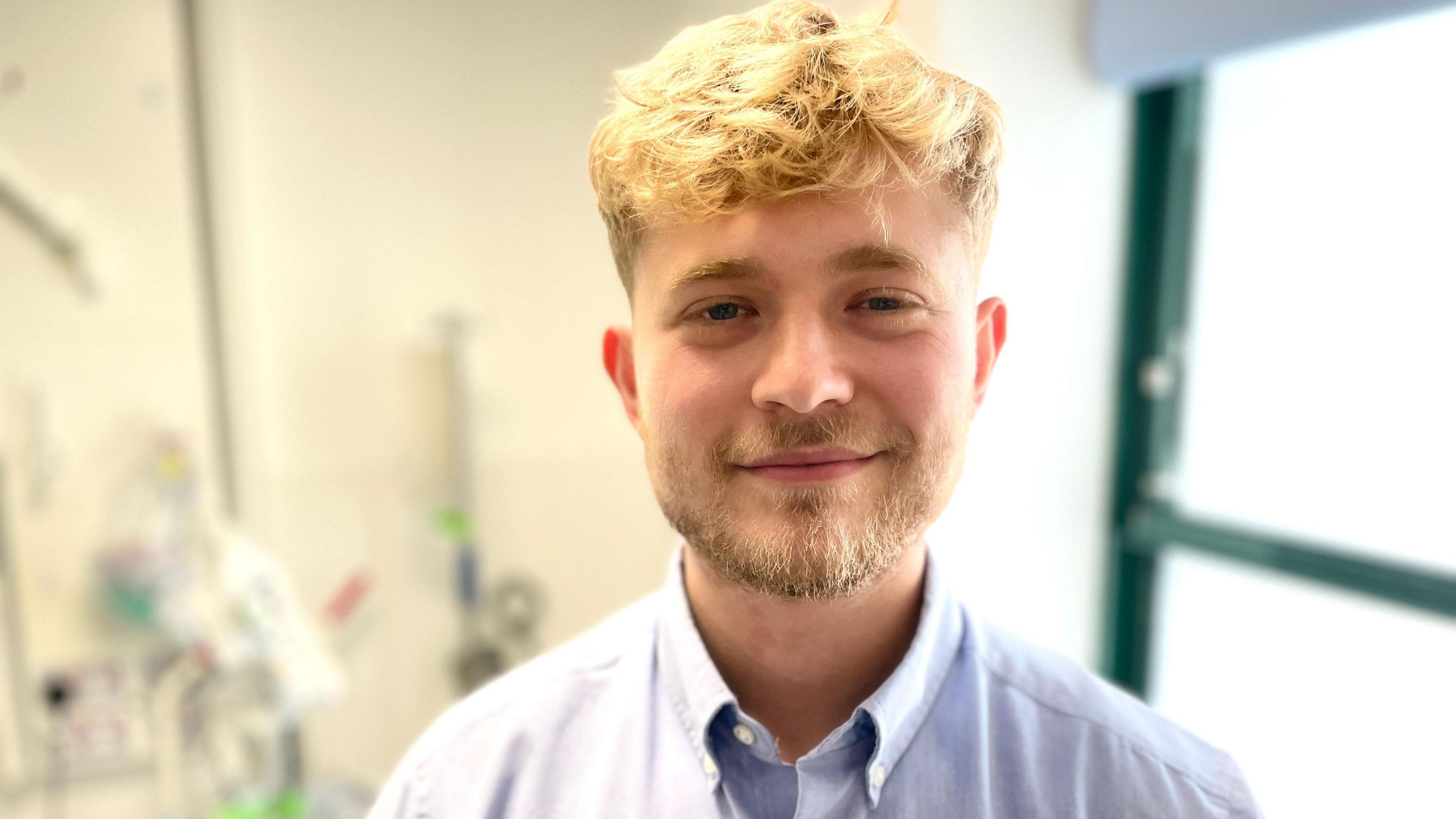 A young man with blonde hair and a beard, wearing a blue shirt.