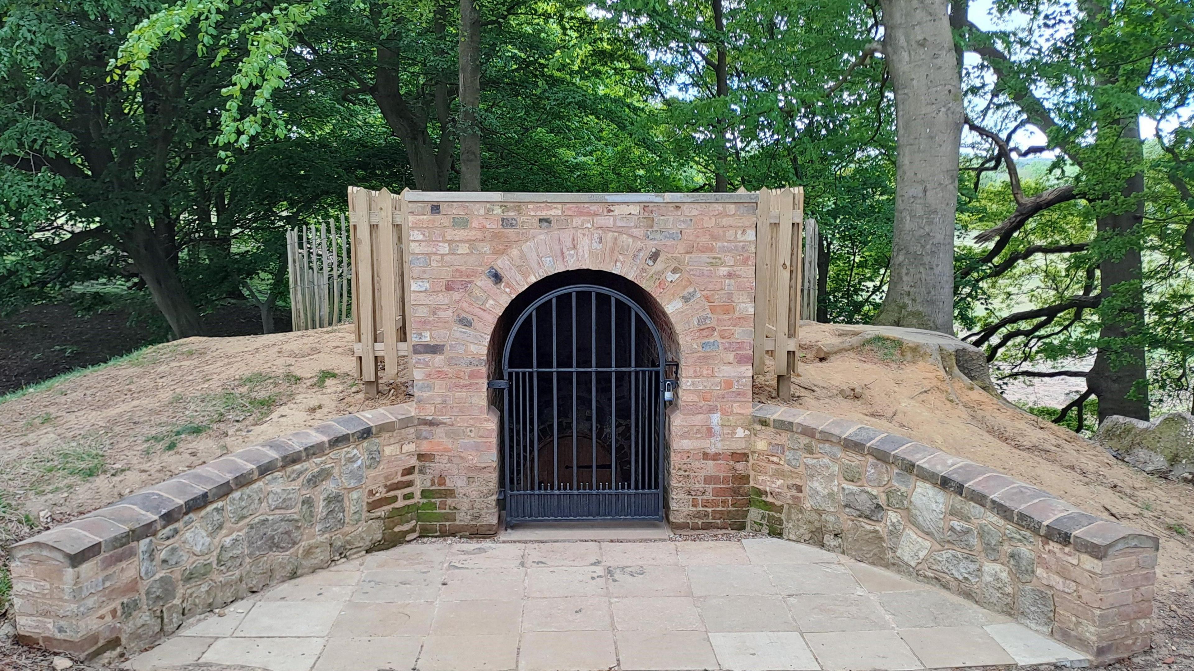 The entrance to Knole icehouse as seen after reconstruction has taken place. The entrance is behind a black gate.
