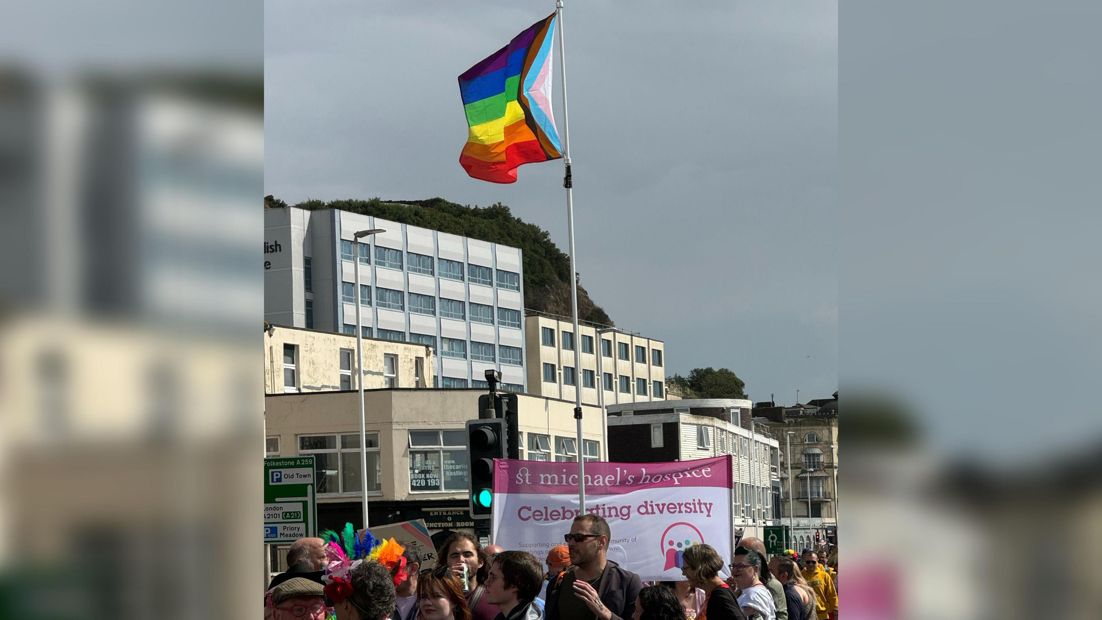 A pride flag is flying above a banner which reads "St Michael's Hospice celebrating diversity" with buildings seen in the background