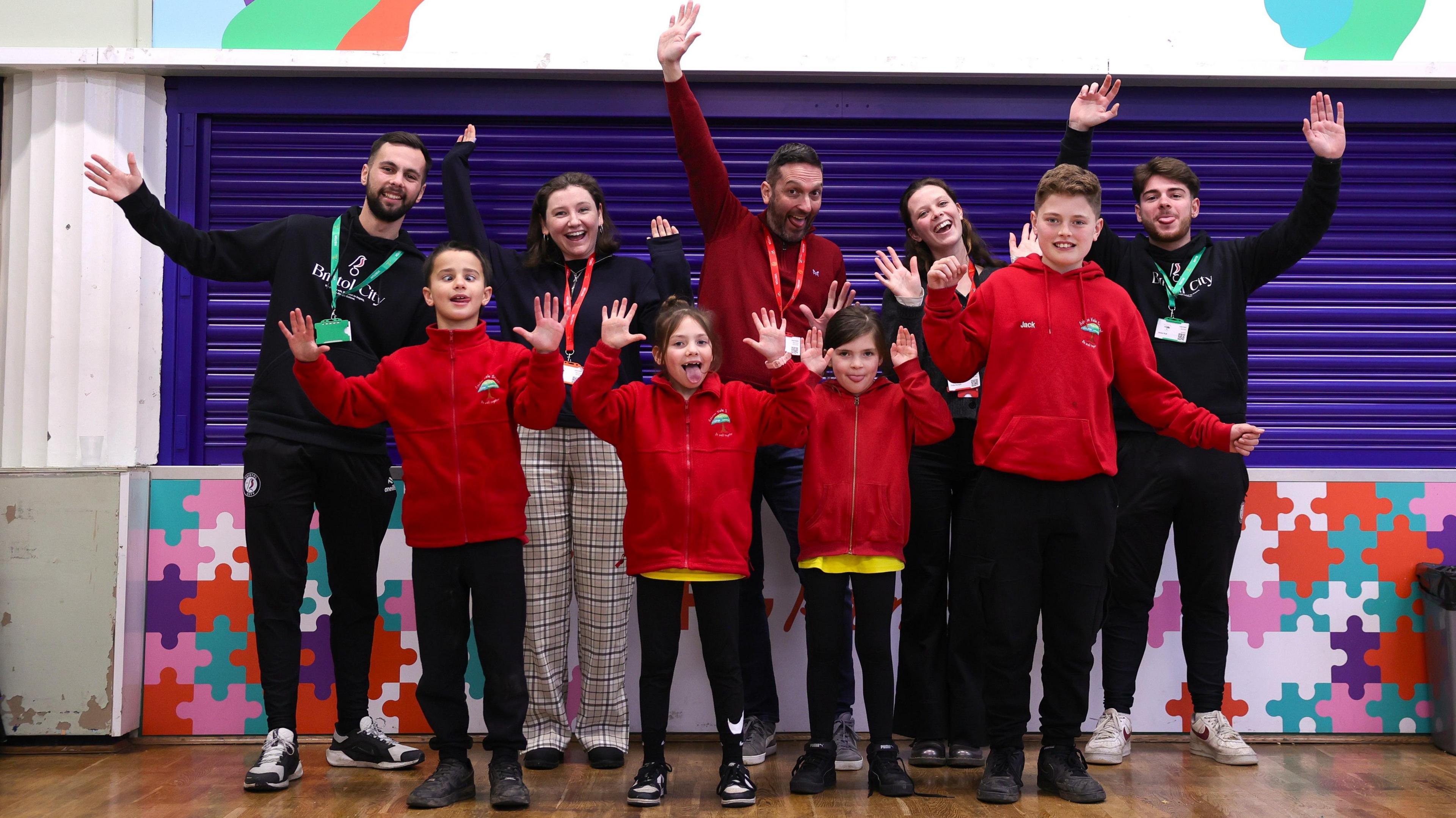 A group of school pupils from Ashton Vale Primary School stand on stage with their arms raised and smiling along with staff from Bristol City during a presentation about preserving wildlife