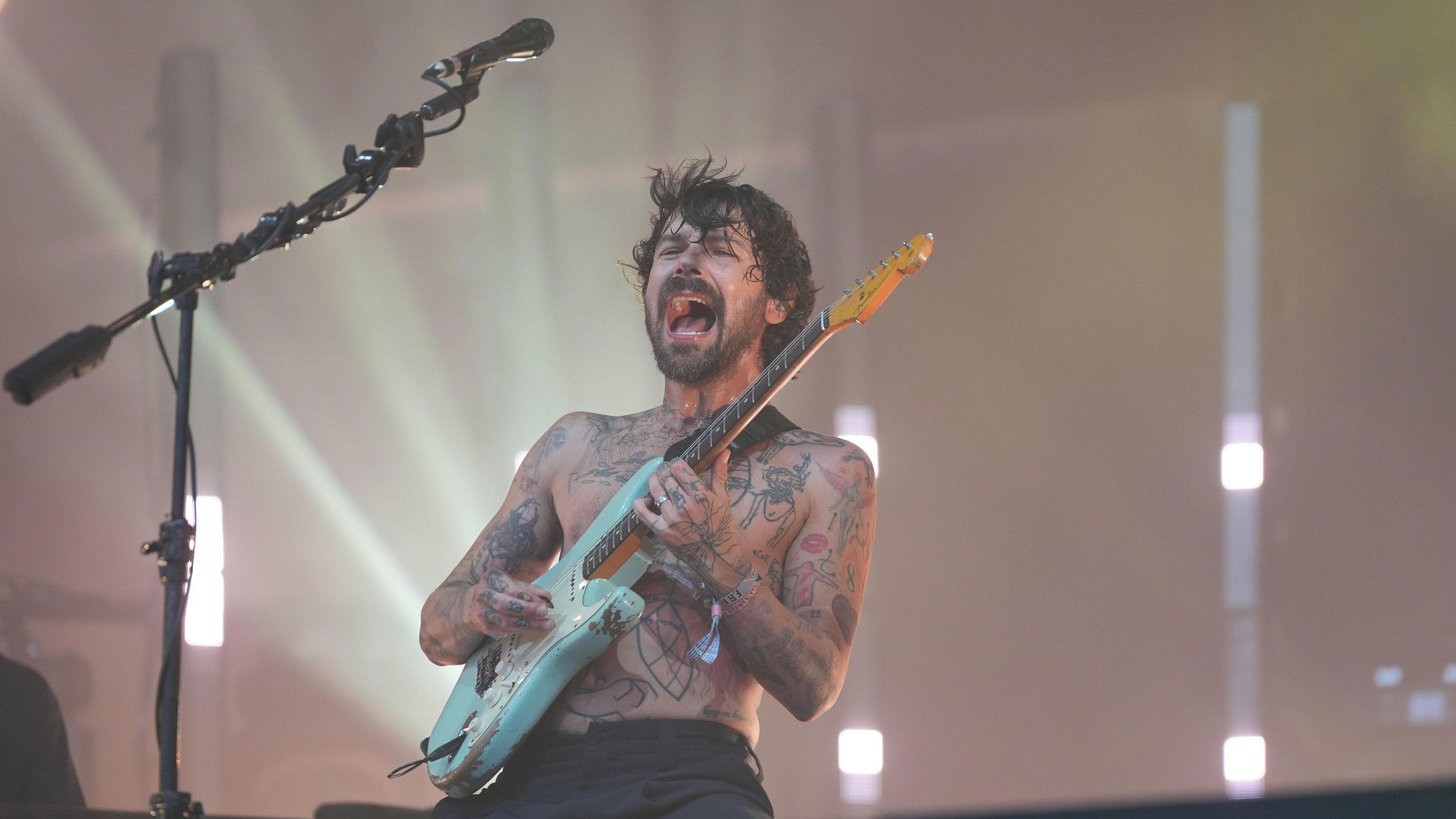 Biffy Clyro singer and guitarist Simon Neil performs onstage he is shirtless, heavily tattooed and playing an aqua coloured Fender Stratocaster guitar.