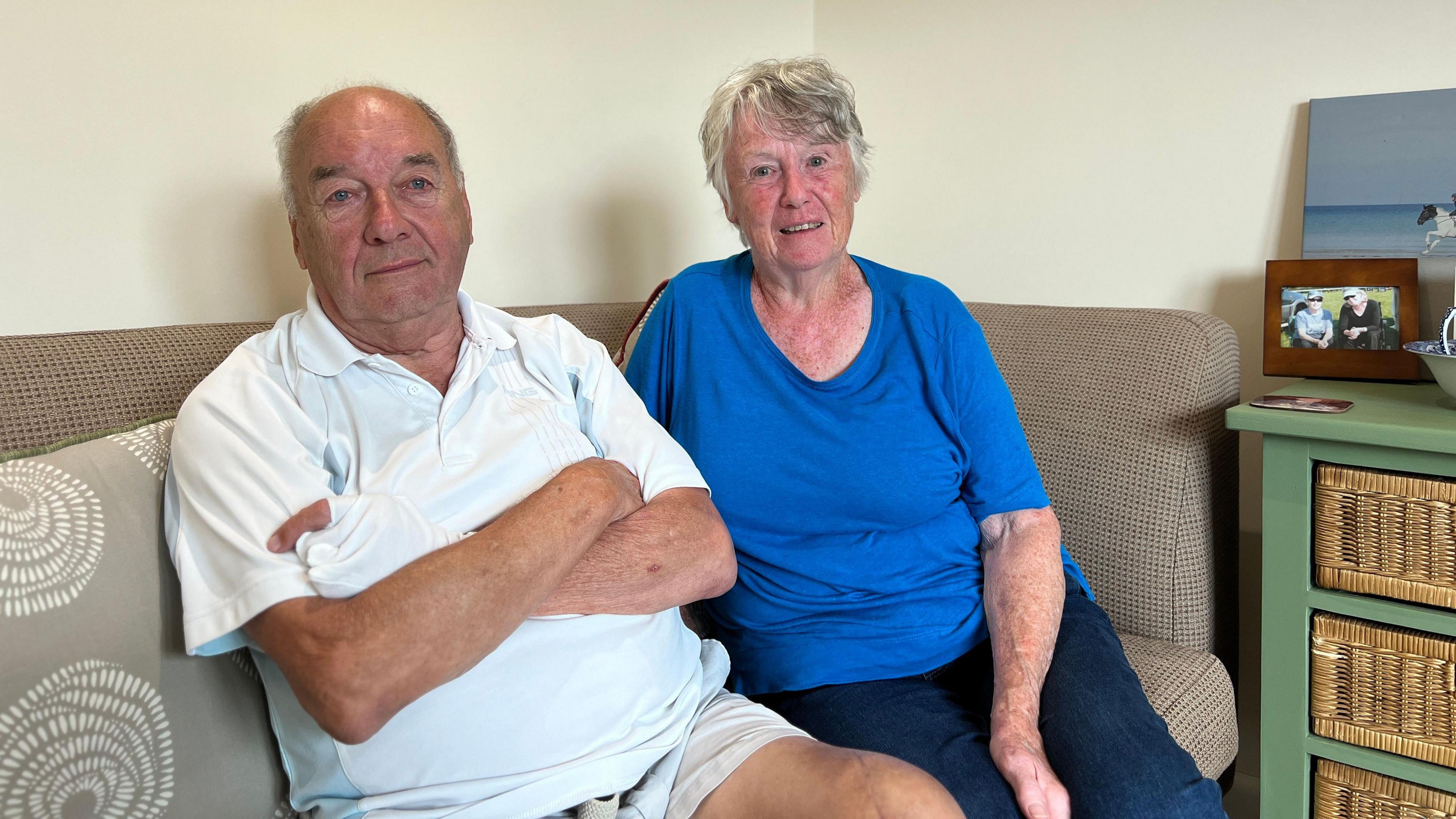 Tony and Evie sit on a grey sofa looking at the camera