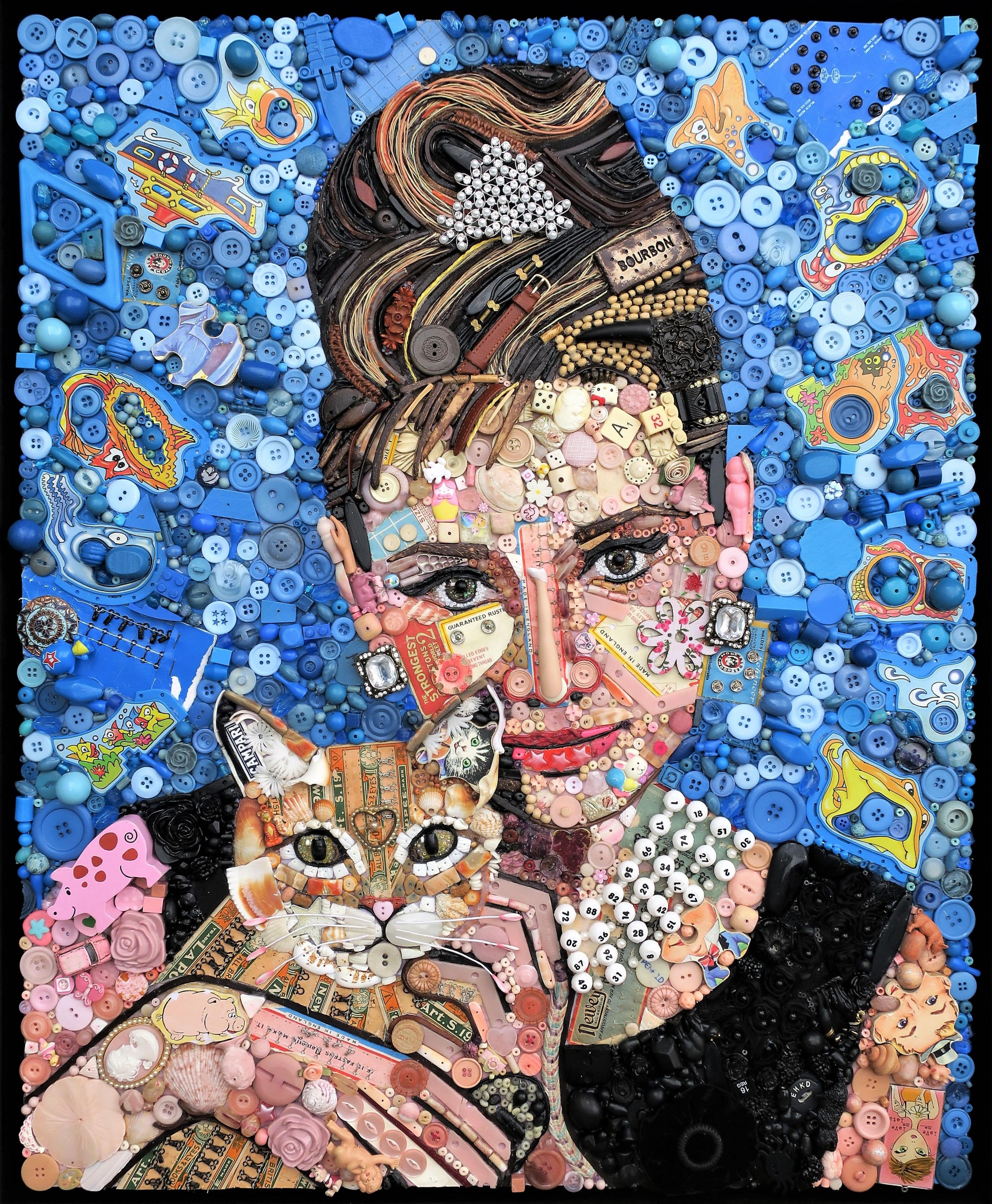 Audrey Hepburn holds a tabby cat. She's wearing a black dress and pearls that look like the might have been made from the keys of a typewriter or calculator. She's set against a brilliant blue background of mainly buttons.