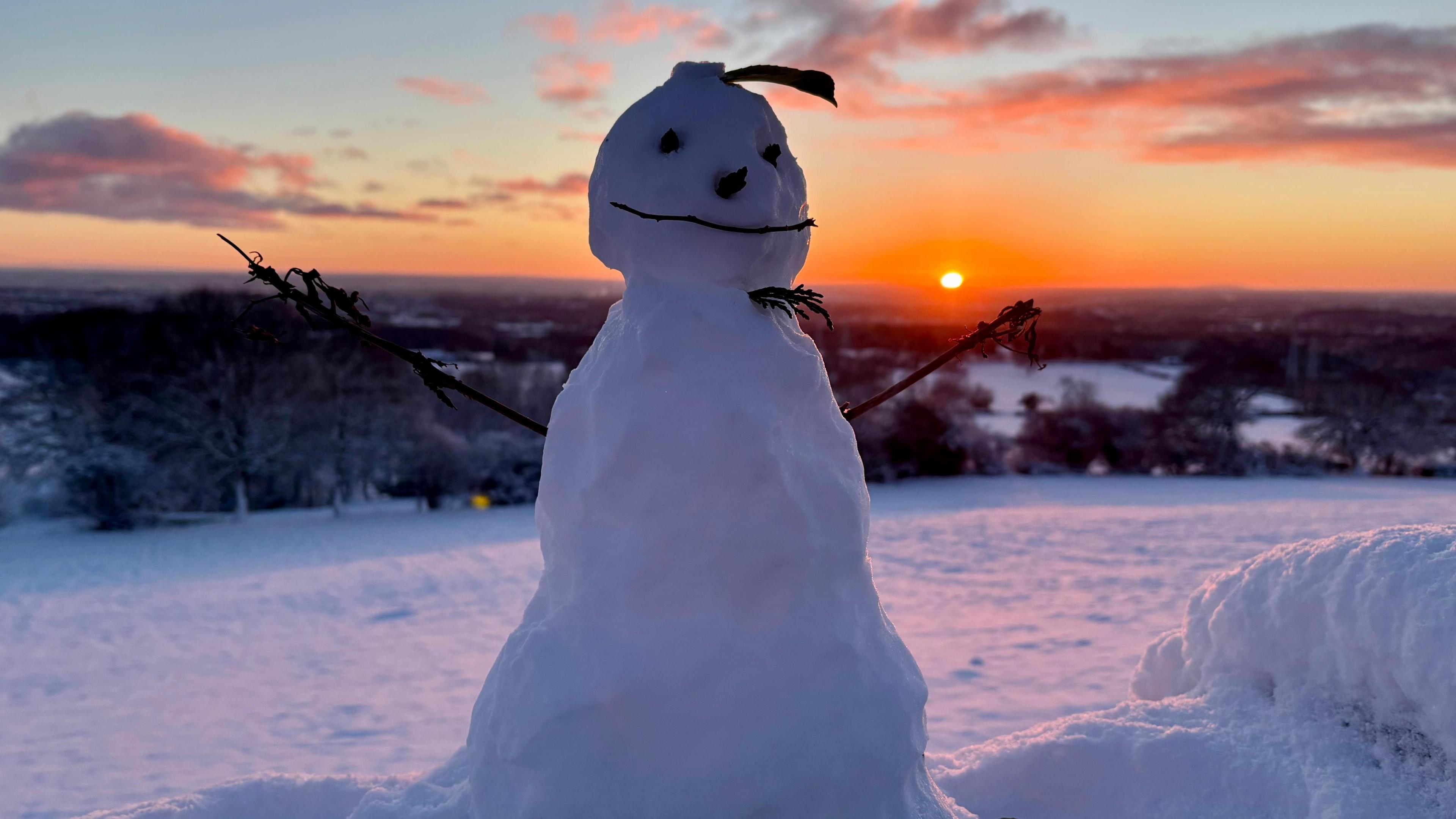 Snowman with smiley face in front of an orange sunrise