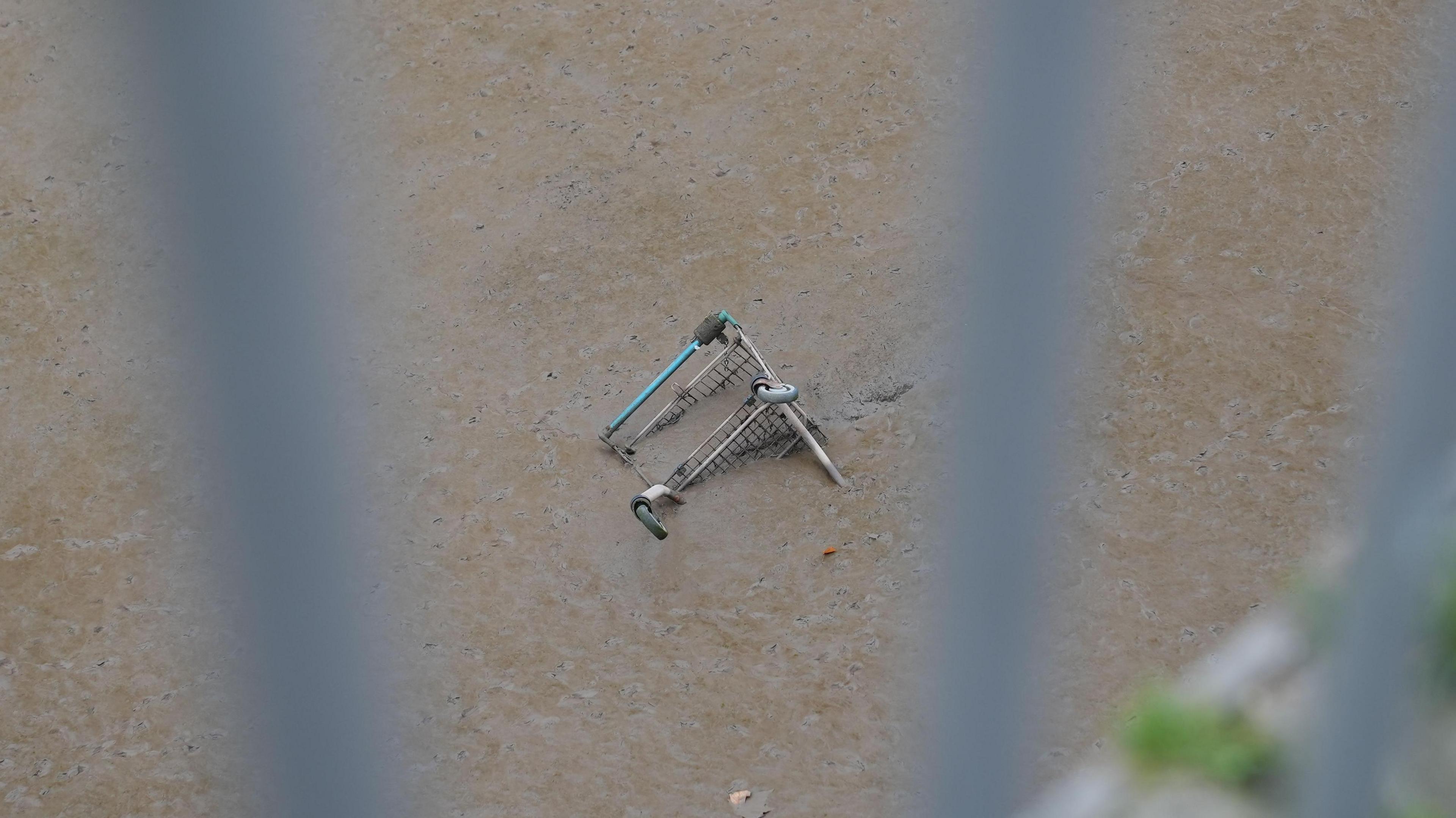 A trolley half buried in mud on the river Usk. the picture is taken through railings.