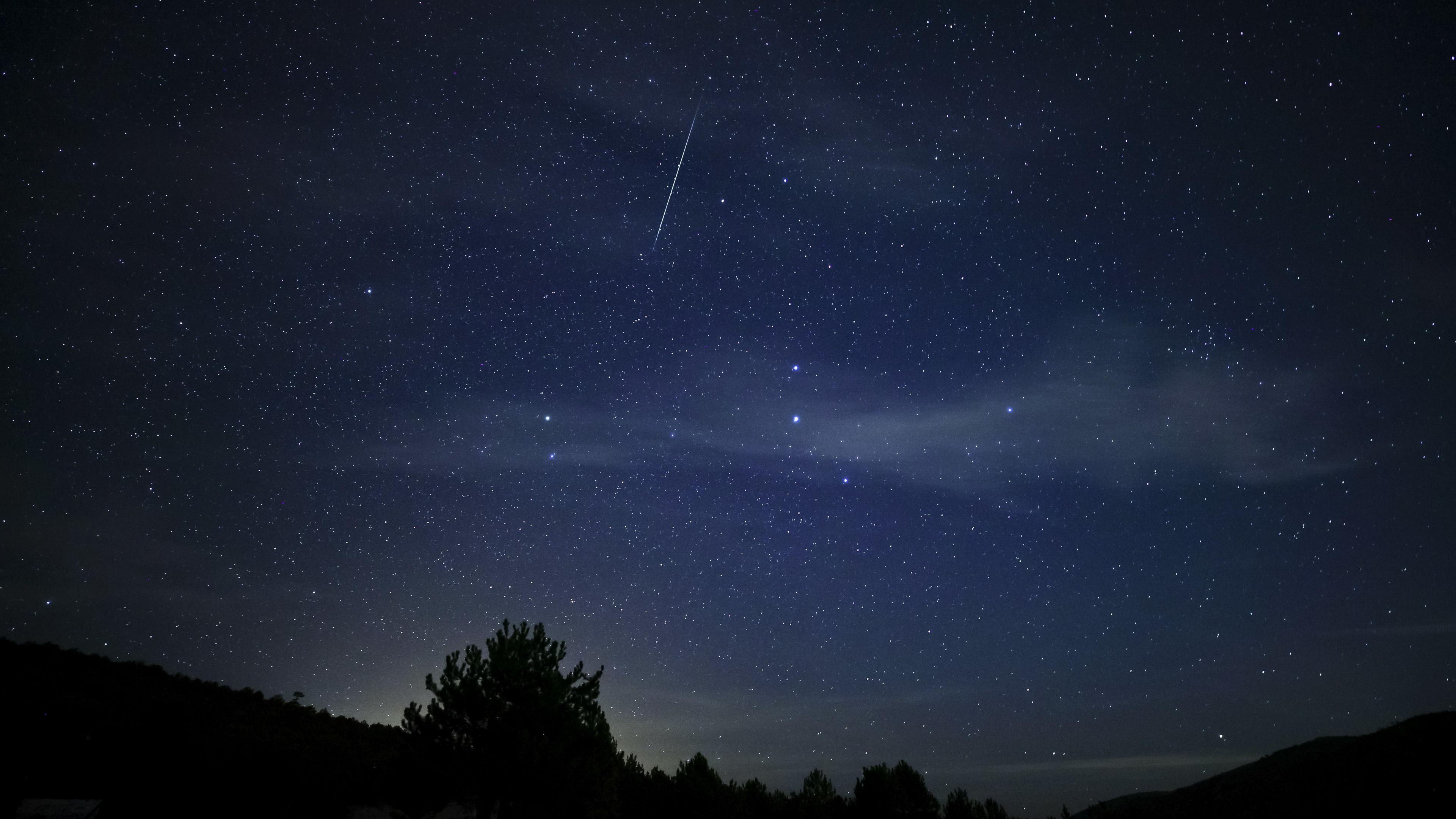 Dark blue night sky illuminated with a few stars and a single meteor streak