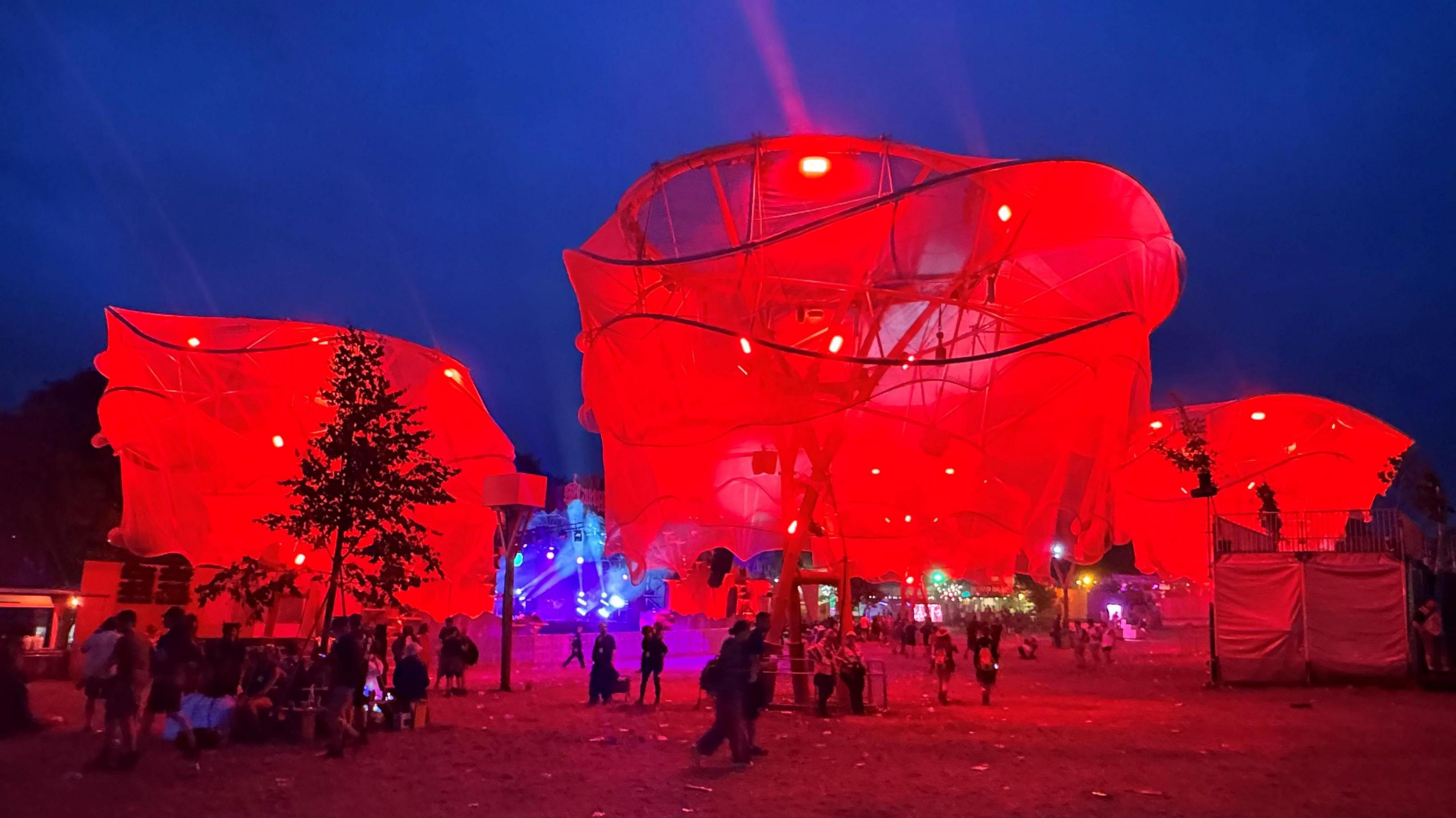 Three large paper trees lit up in red in the Shangri-La area of Glastonbury Festival.