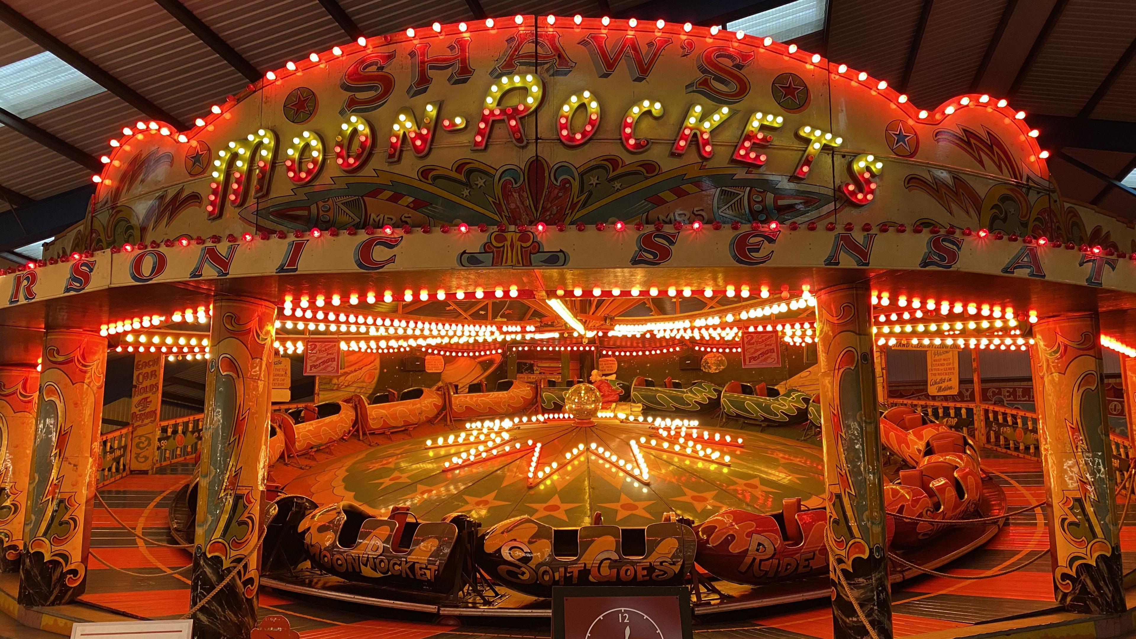 A fairground ride called Shaw's Moon-Rockets which features rockets that two people can sit in. They are placed in a circle and move clockwise. The ride is highly decorated with stars and swirls and there are lightbulbs in a star shape and throughout. 