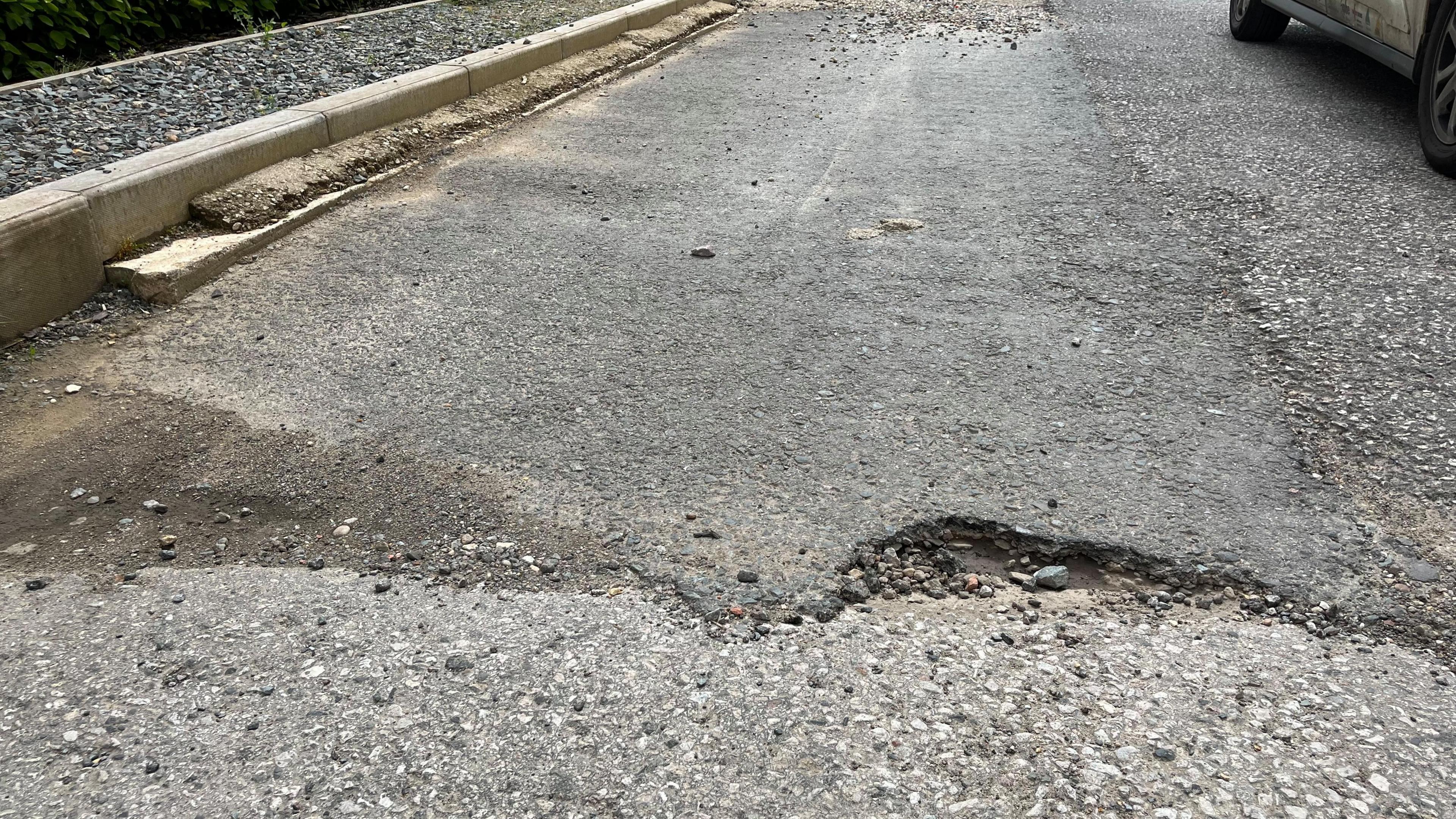 Potholes and bumpy, stony road surface with uneven curb