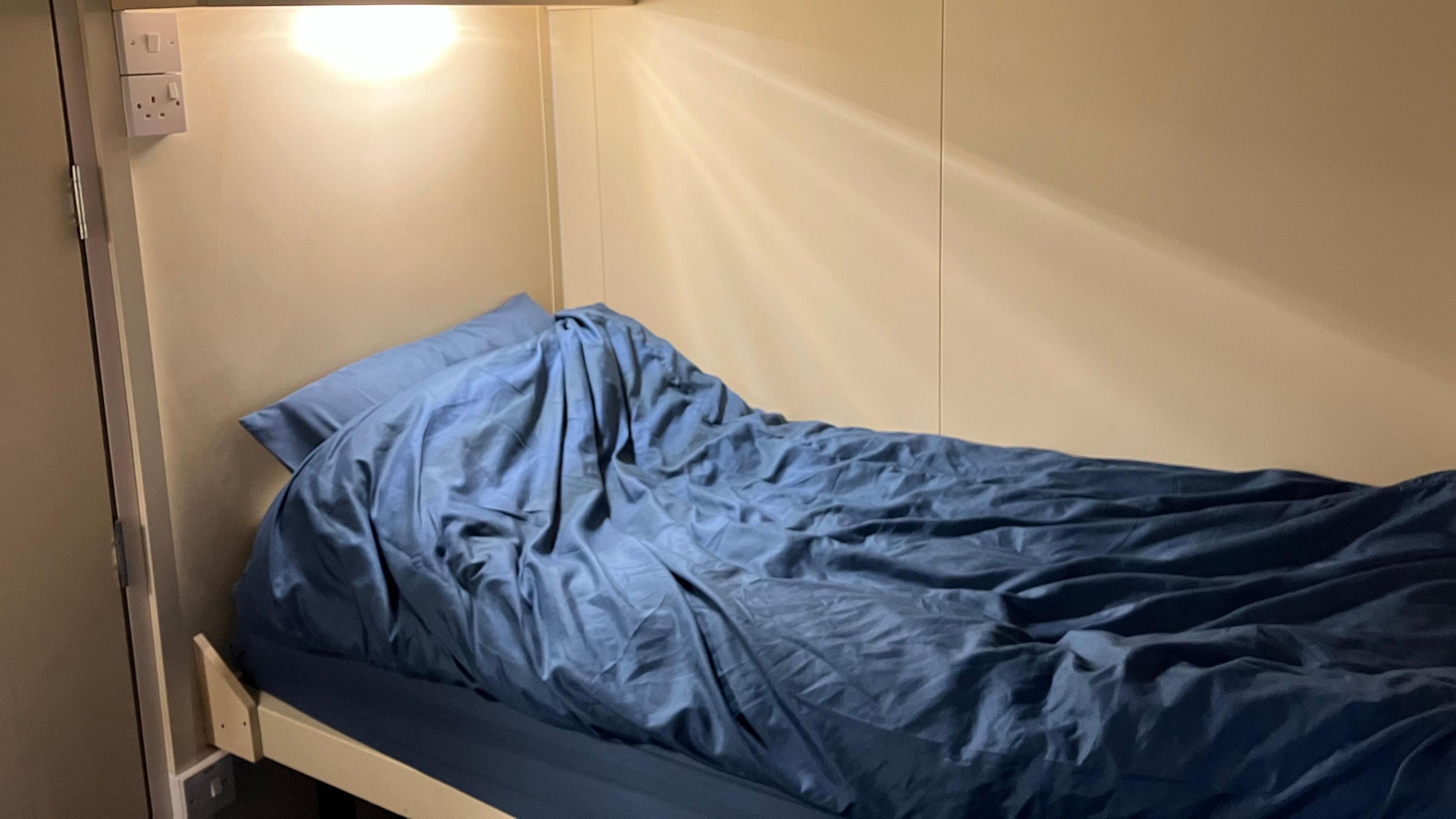 Inside the sleeper pod, there is a single bed with a blue duvet, pillow and mattress. 